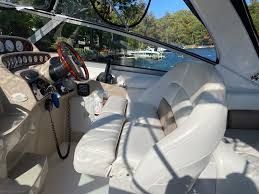 Interior of a boat with white seats and a steering wheel, surrounded by water and trees.