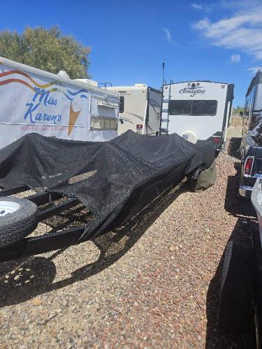 A boat trailer with a black cover is parked on a gravel lot next to RVs.