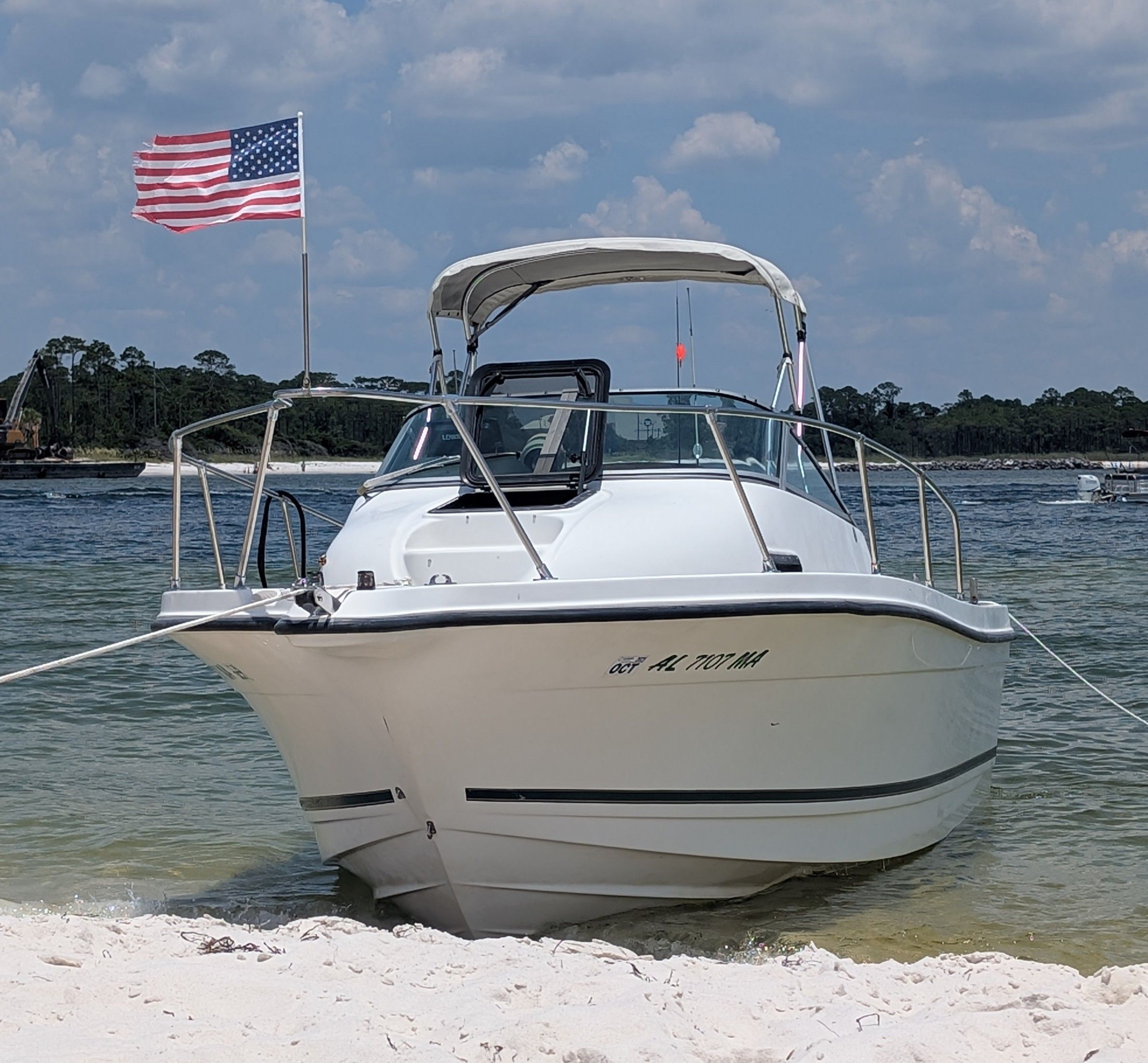 A 2001 Trophy Bayliner boat is anchored on the beach. An American flag waves in the background.