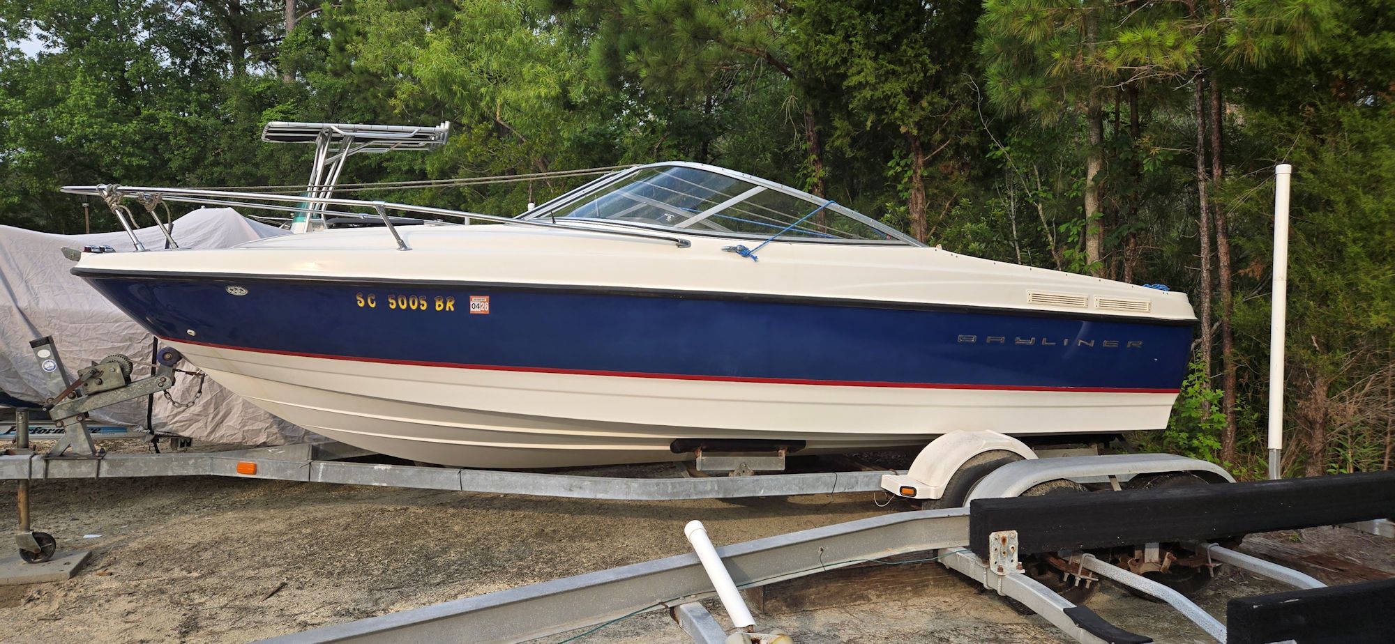 2004 Bayliner B210 Classic on trailer in wooded area.