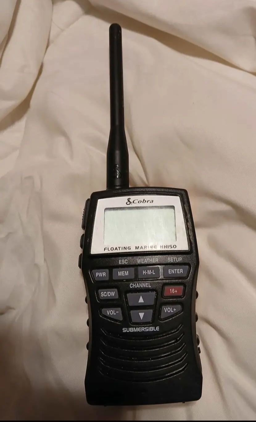 A Cobra marine radio with an antenna rests on a white cloth.
