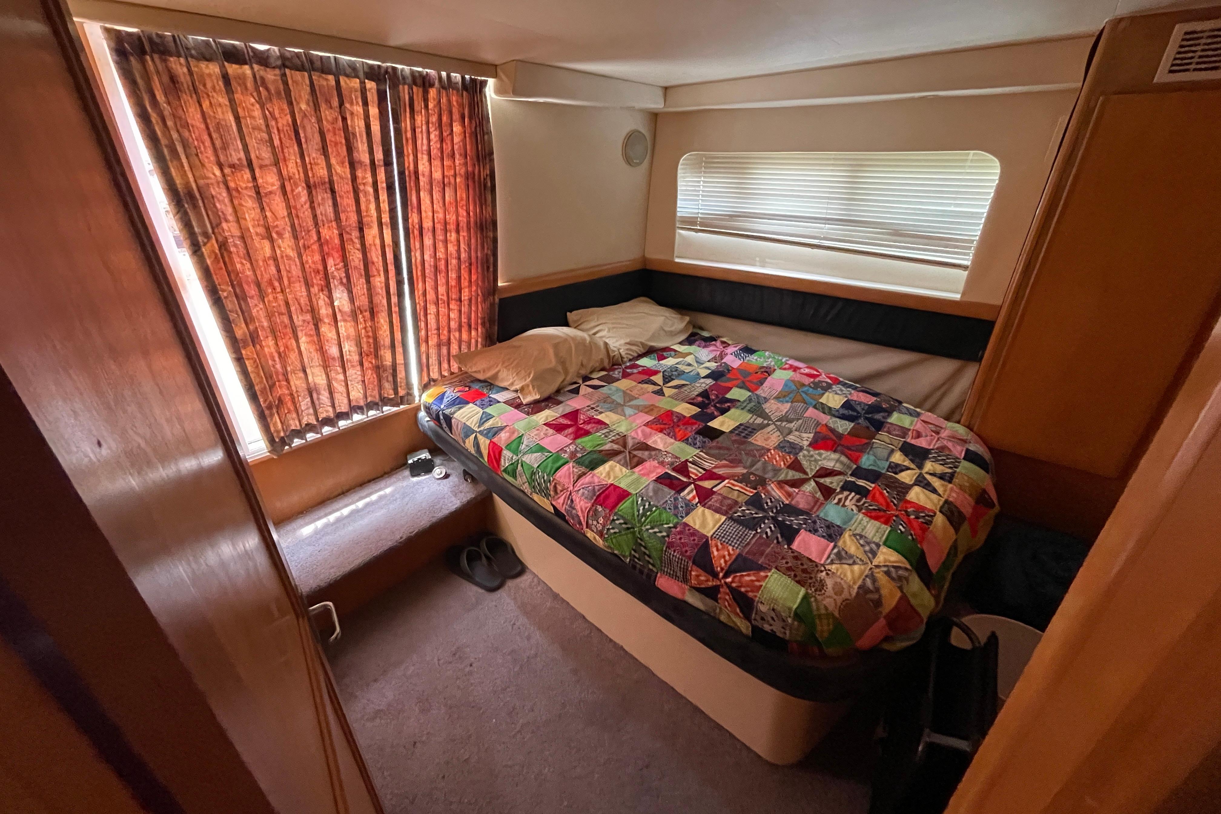 Cozy bedroom in 1996 Carver 400 Cockpit Motor Yacht with colorful quilt and window blinds.
