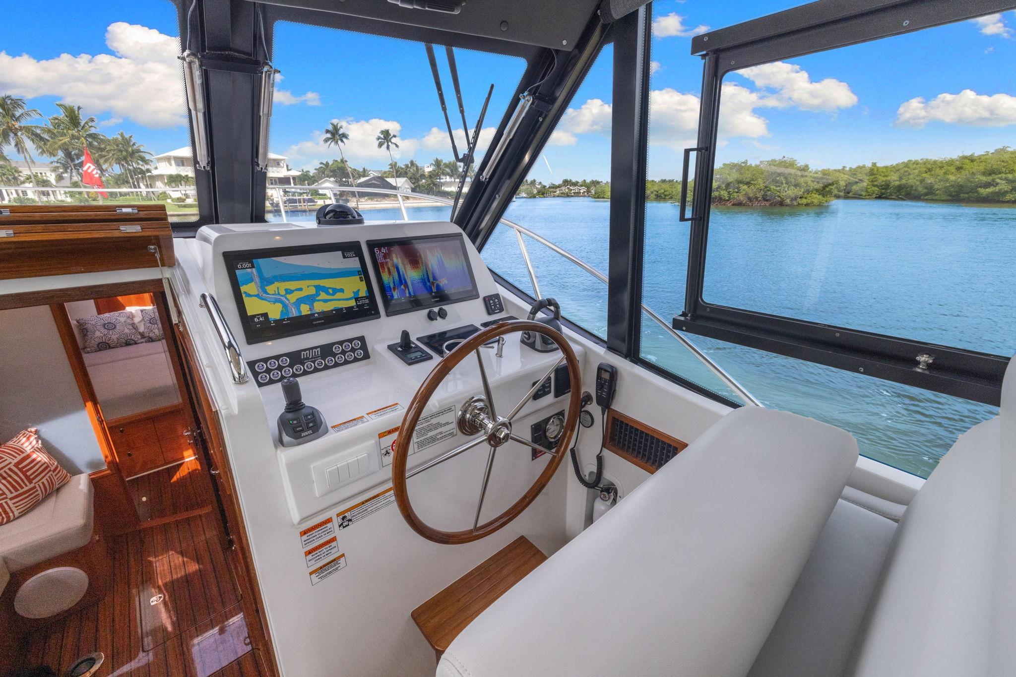 2024 MJM 42 yacht helm with navigation screens, overlooking serene waterway and lush greenery.