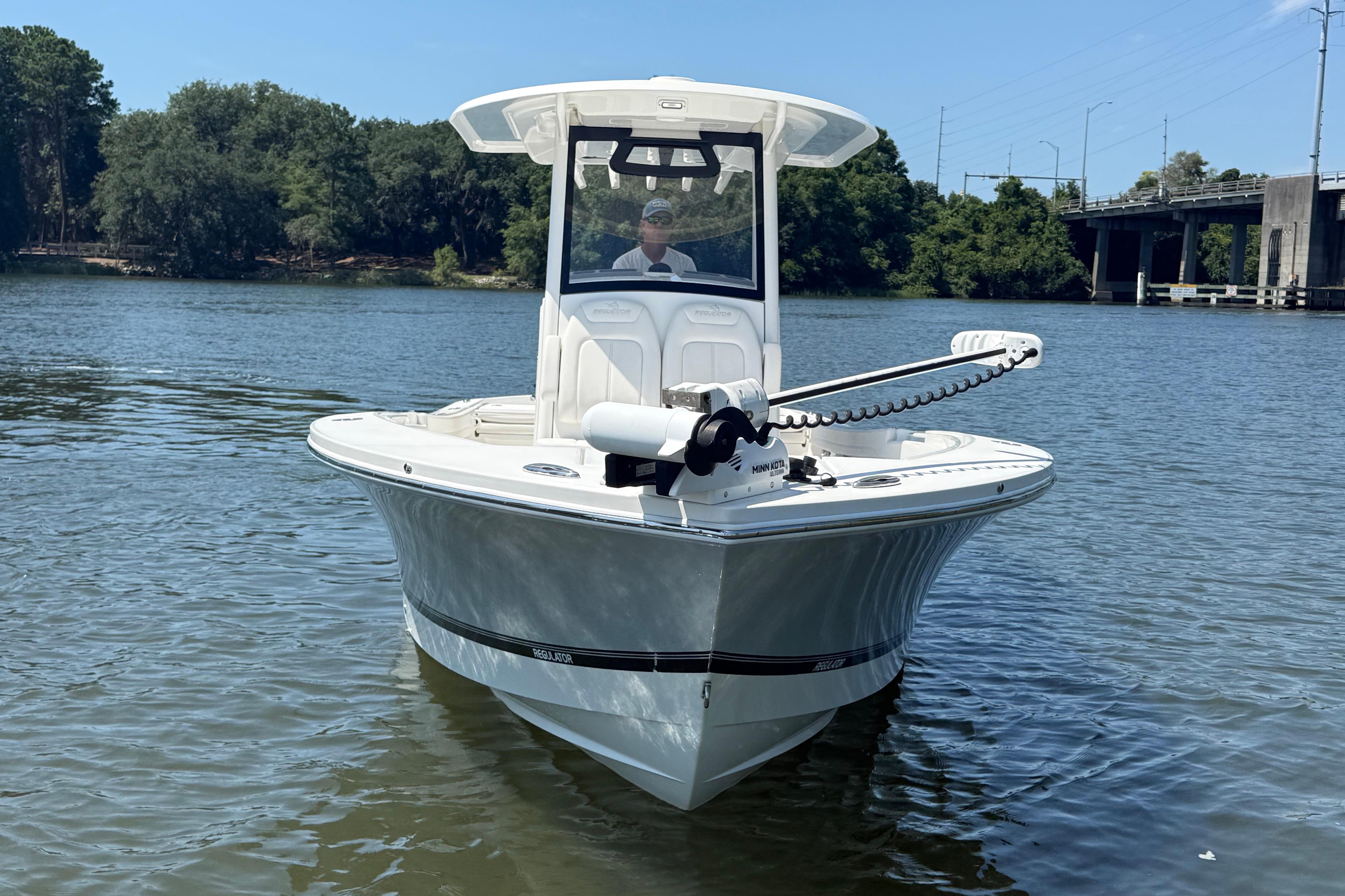 2023 Regulator 26XO boat on calm water near a bridge and trees.