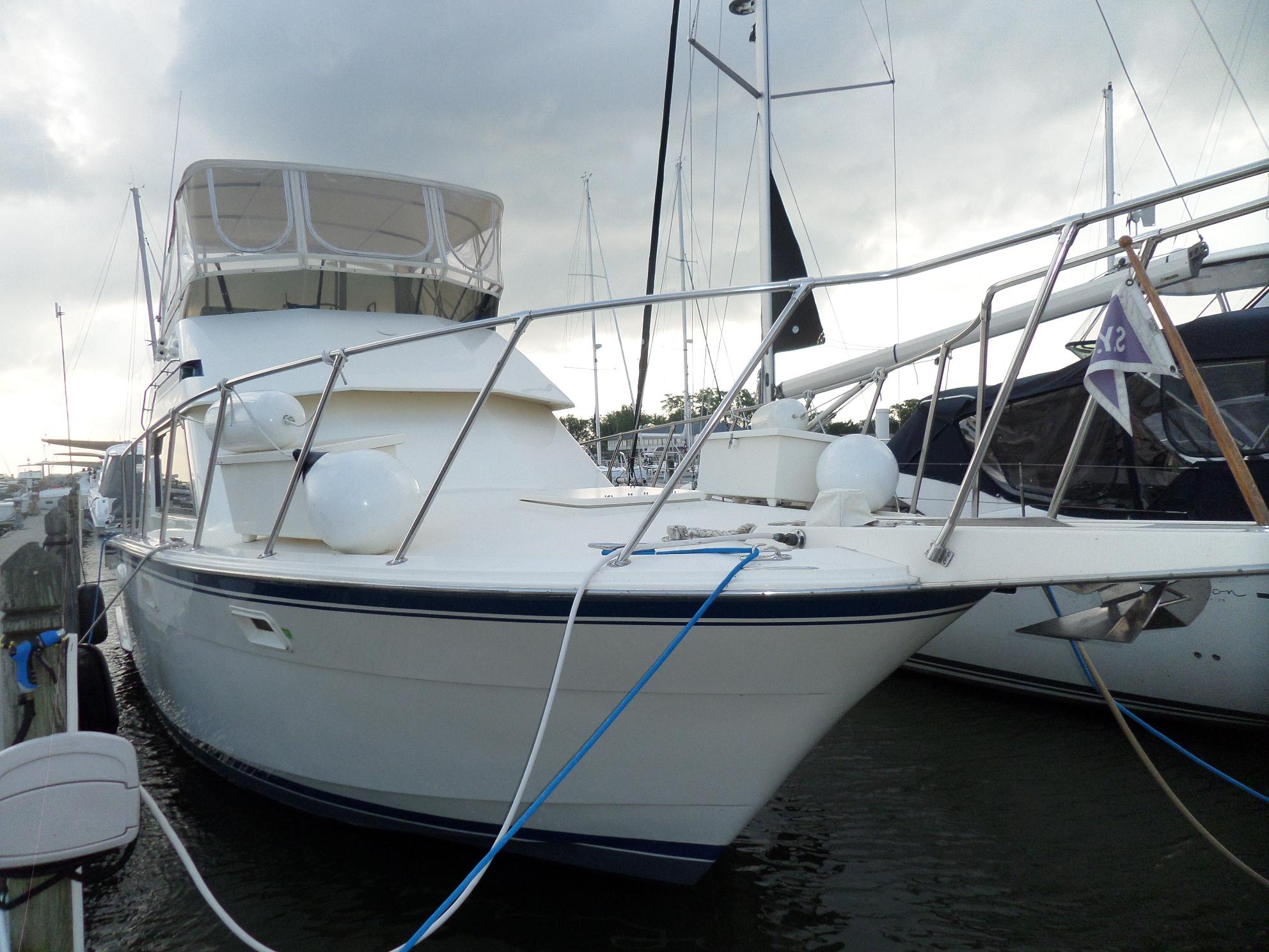 1987 Hatteras 42 Convertible yacht docked at marina under cloudy sky.