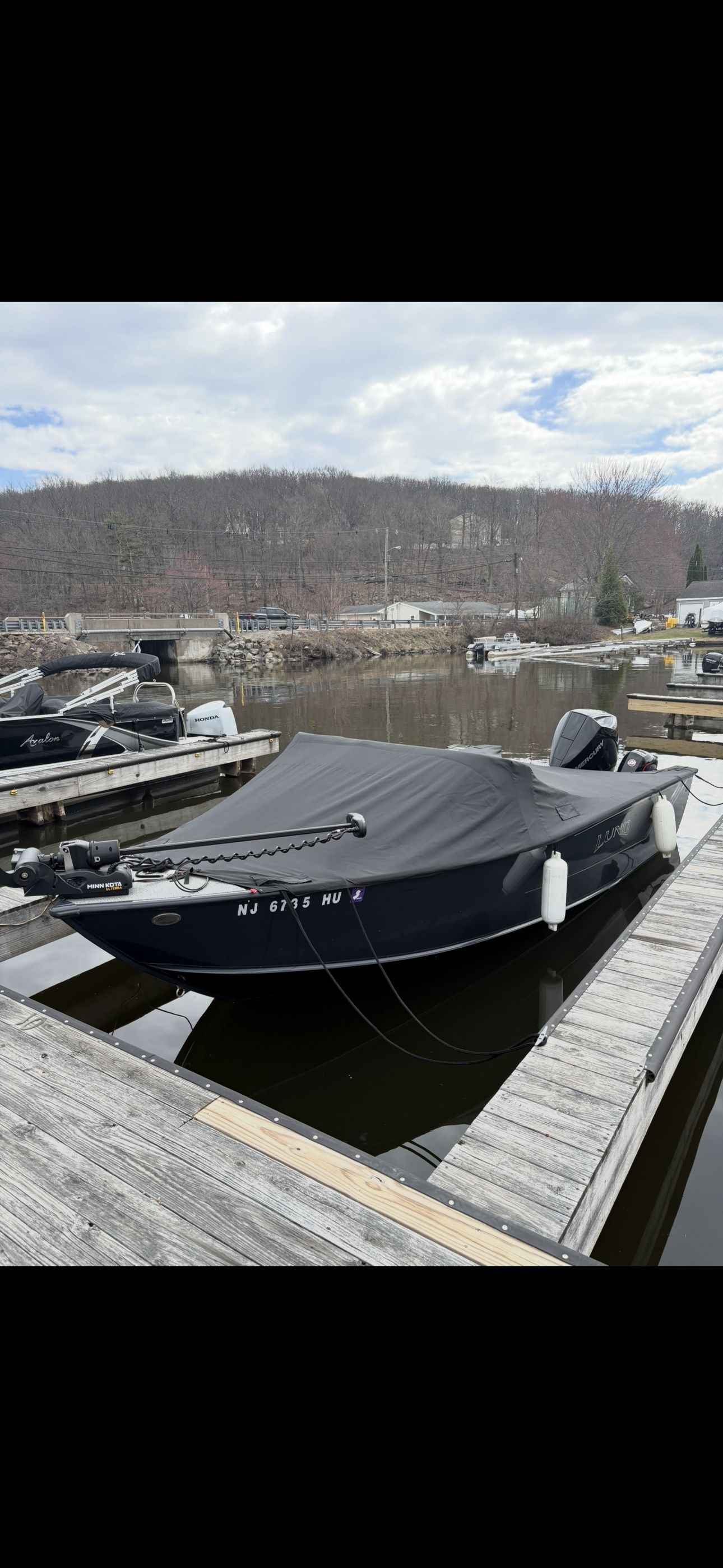 A Lund Fisherman 2075 boat is docked, covered, with fenders attached.