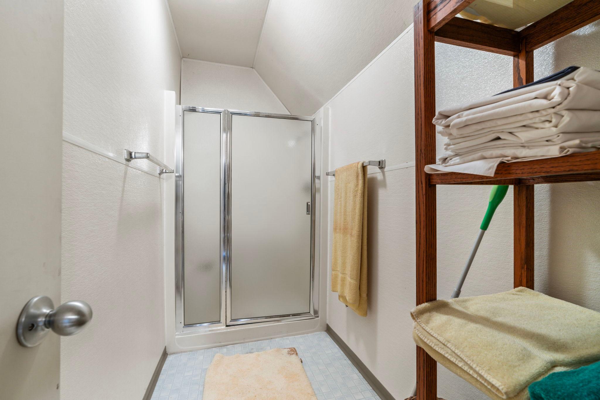 Small bathroom with shower, wooden shelving, and towels in a 1976 Custom Boathouse.