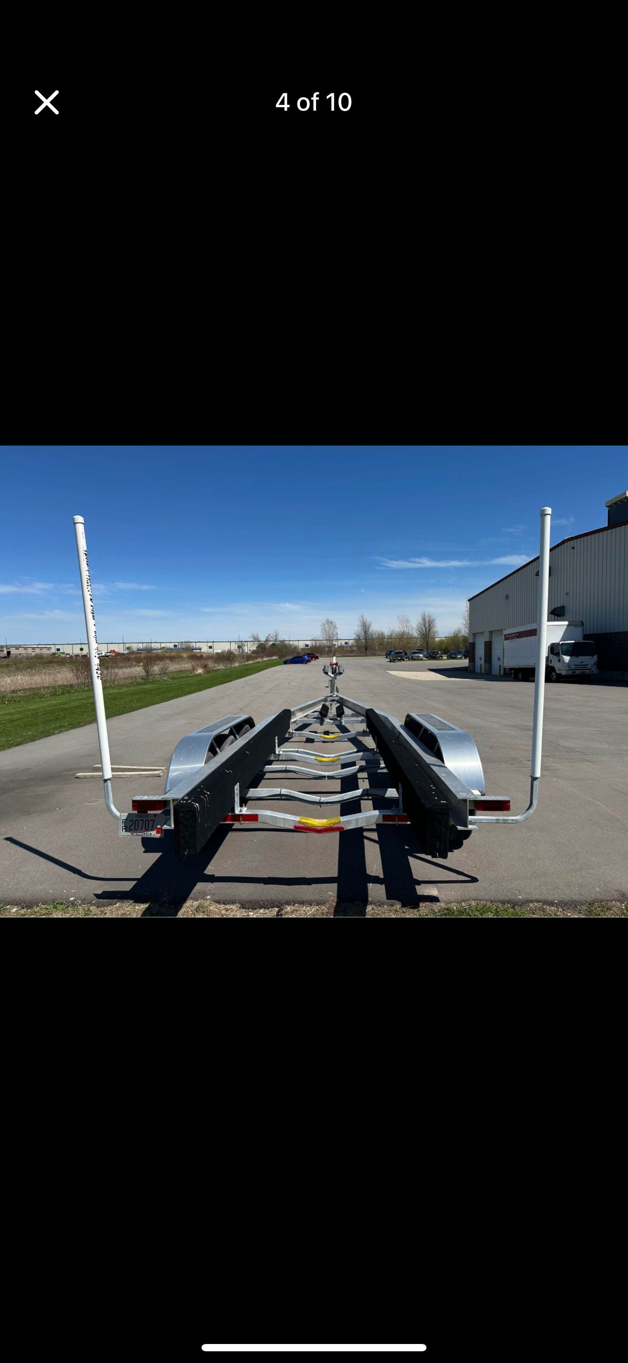 A boat trailer sits on a paved path next to a building under a clear sky.