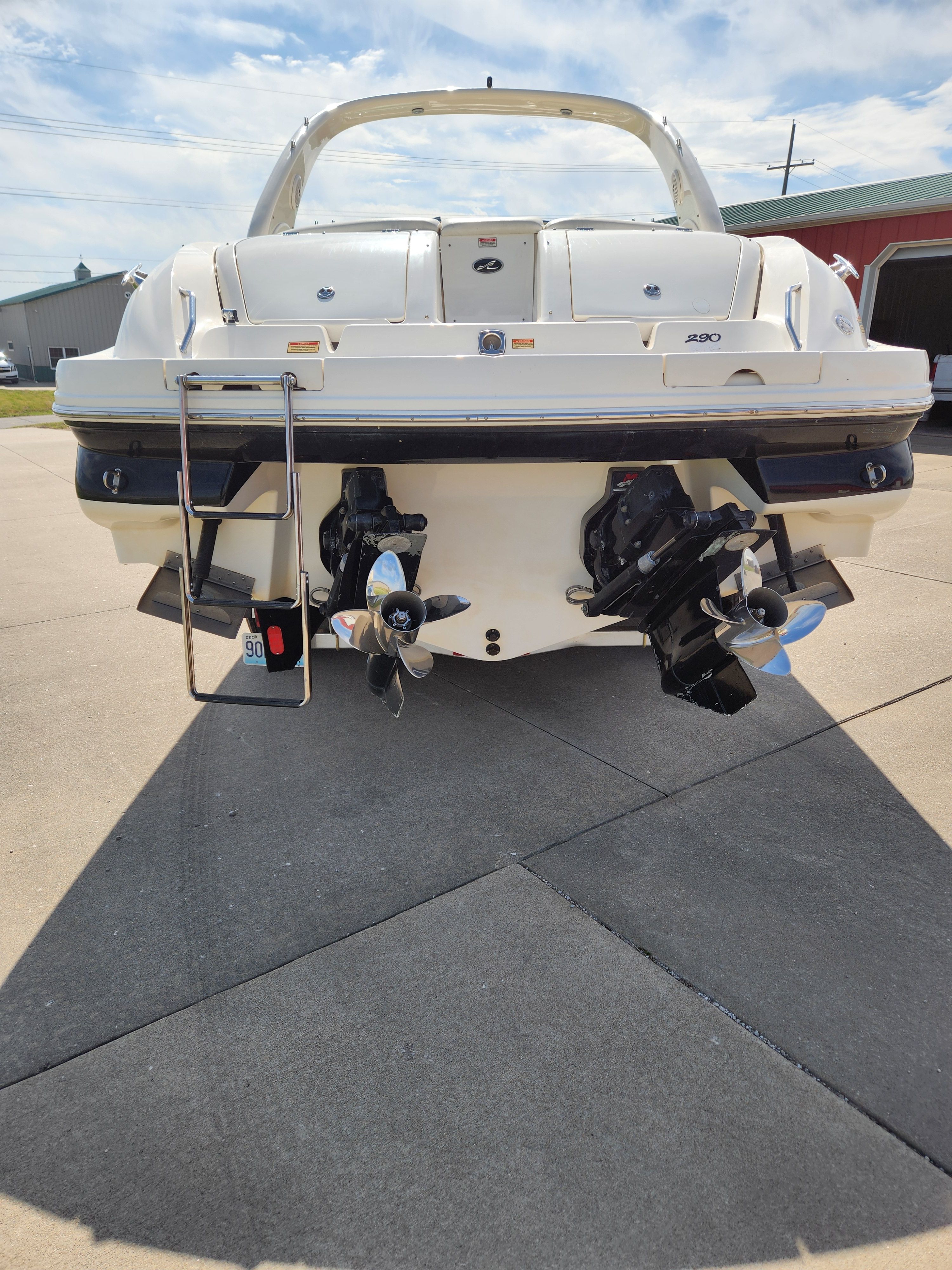 The stern of a white Sea Ray 290 BR boat with dual propellers and a ladder.