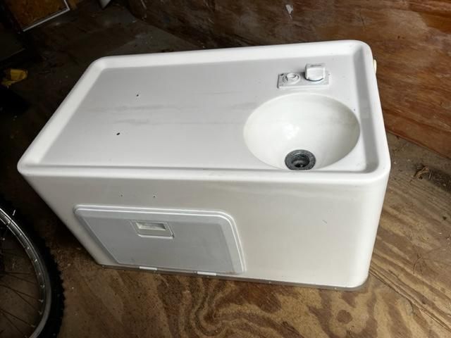 A white sink with a faucet and drain, mounted on a rectangular base.
