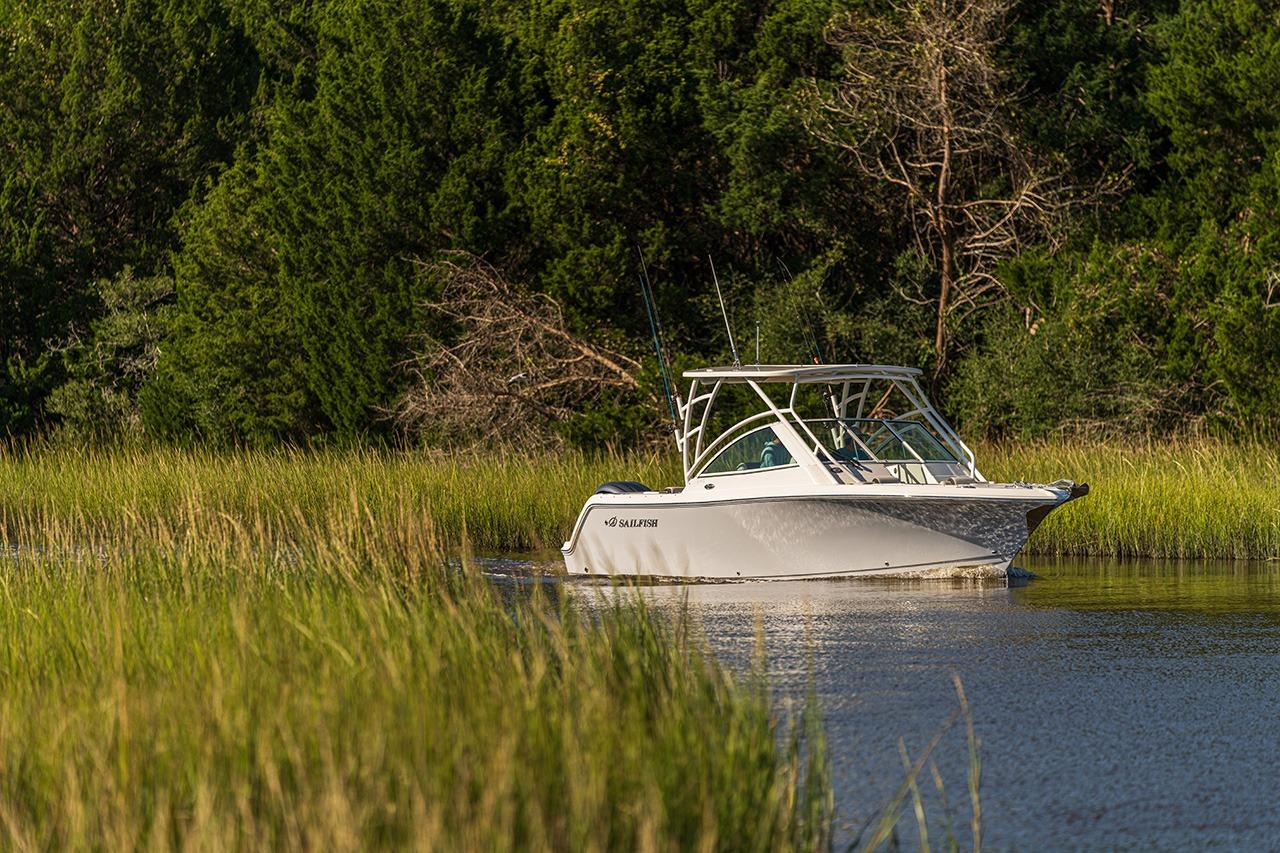 2026 Sailfish 245 DC boat cruising through lush, green waterside vegetation.