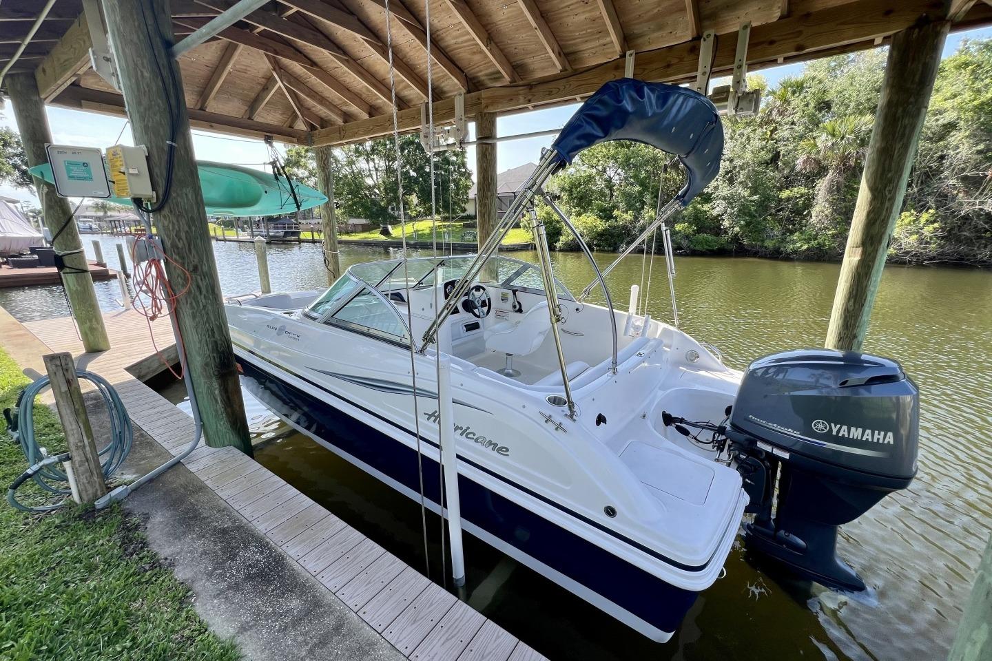 2013 Hurricane SunDeck 187 OB boat docked under a wooden canopy with Yamaha outboard motor.