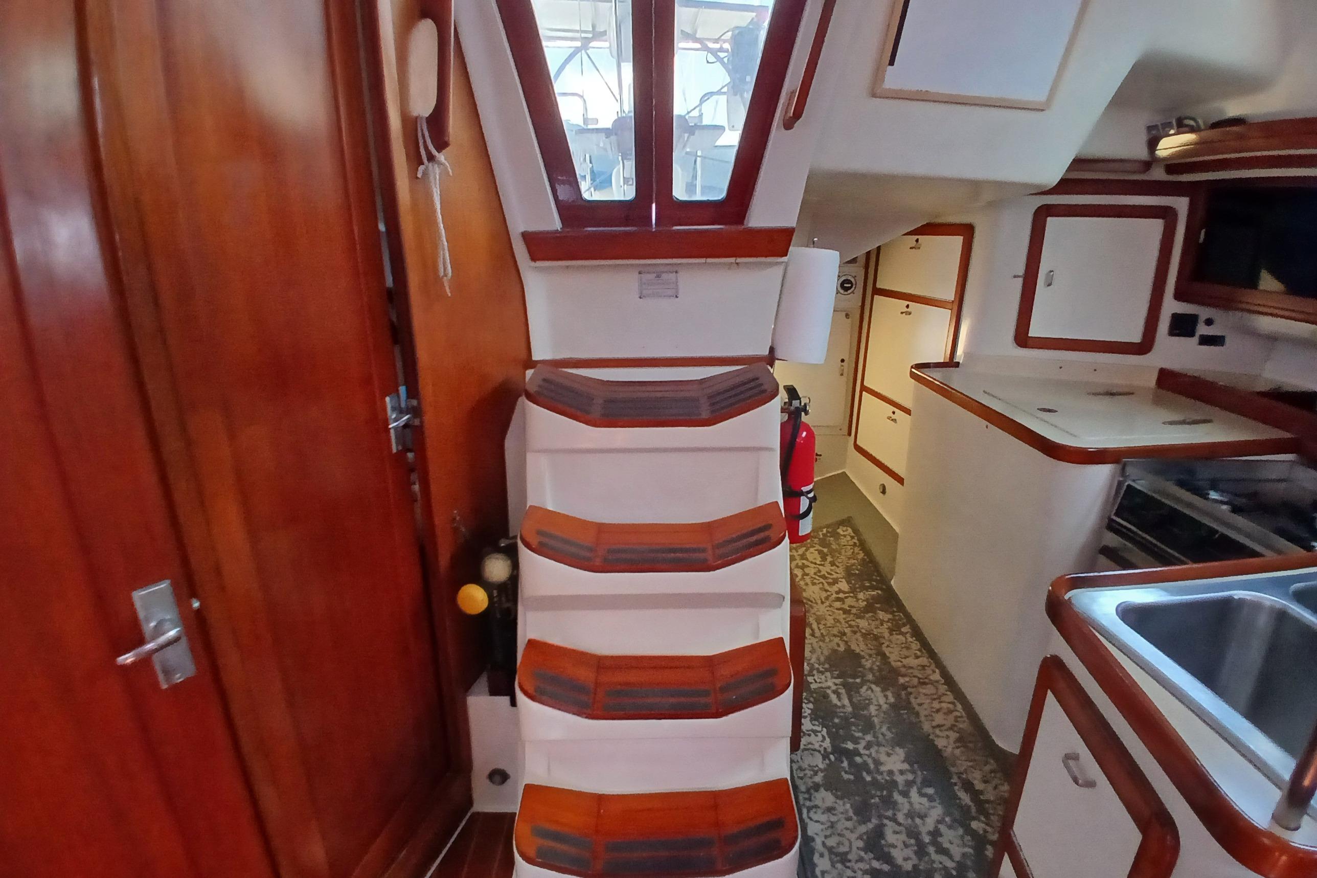 Interior of a 1995 Catalina 42 MkII sailboat, featuring wooden stairs and compact kitchen area.