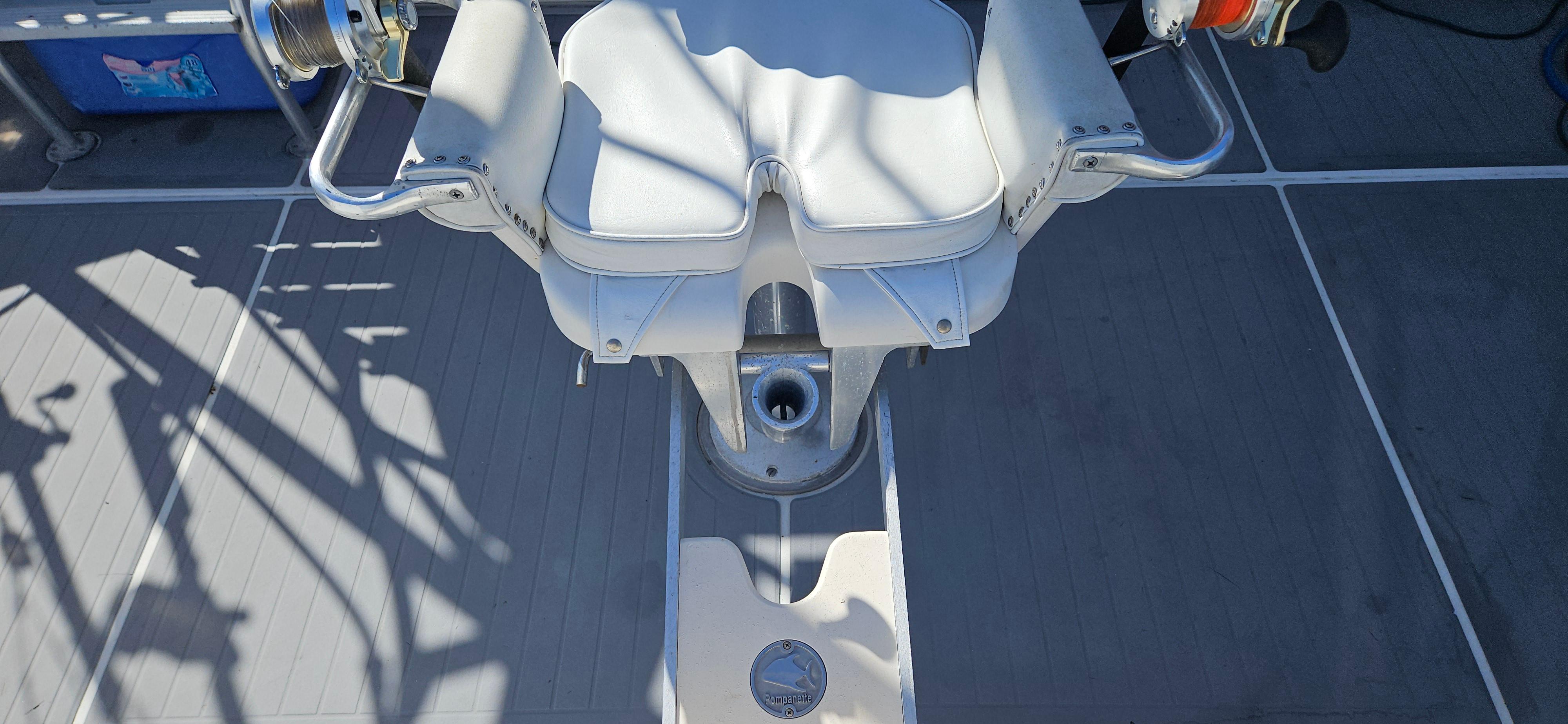 Captain's chair on a 1995 Bertram Convertible boat deck, featuring white upholstery and metal armrests.