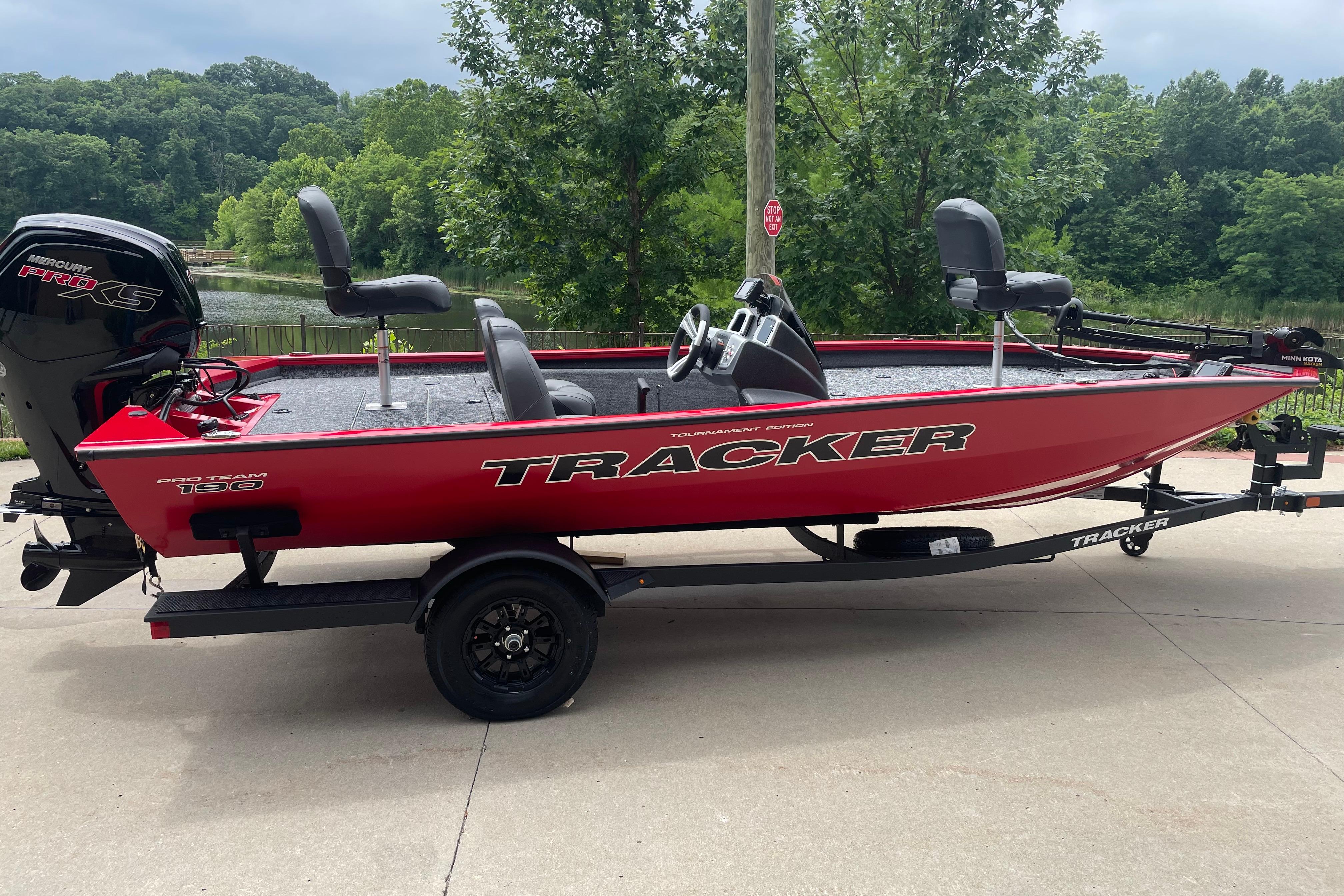 2026 Tracker Pro Team 190 boat in vibrant red, parked outdoors near lush greenery.