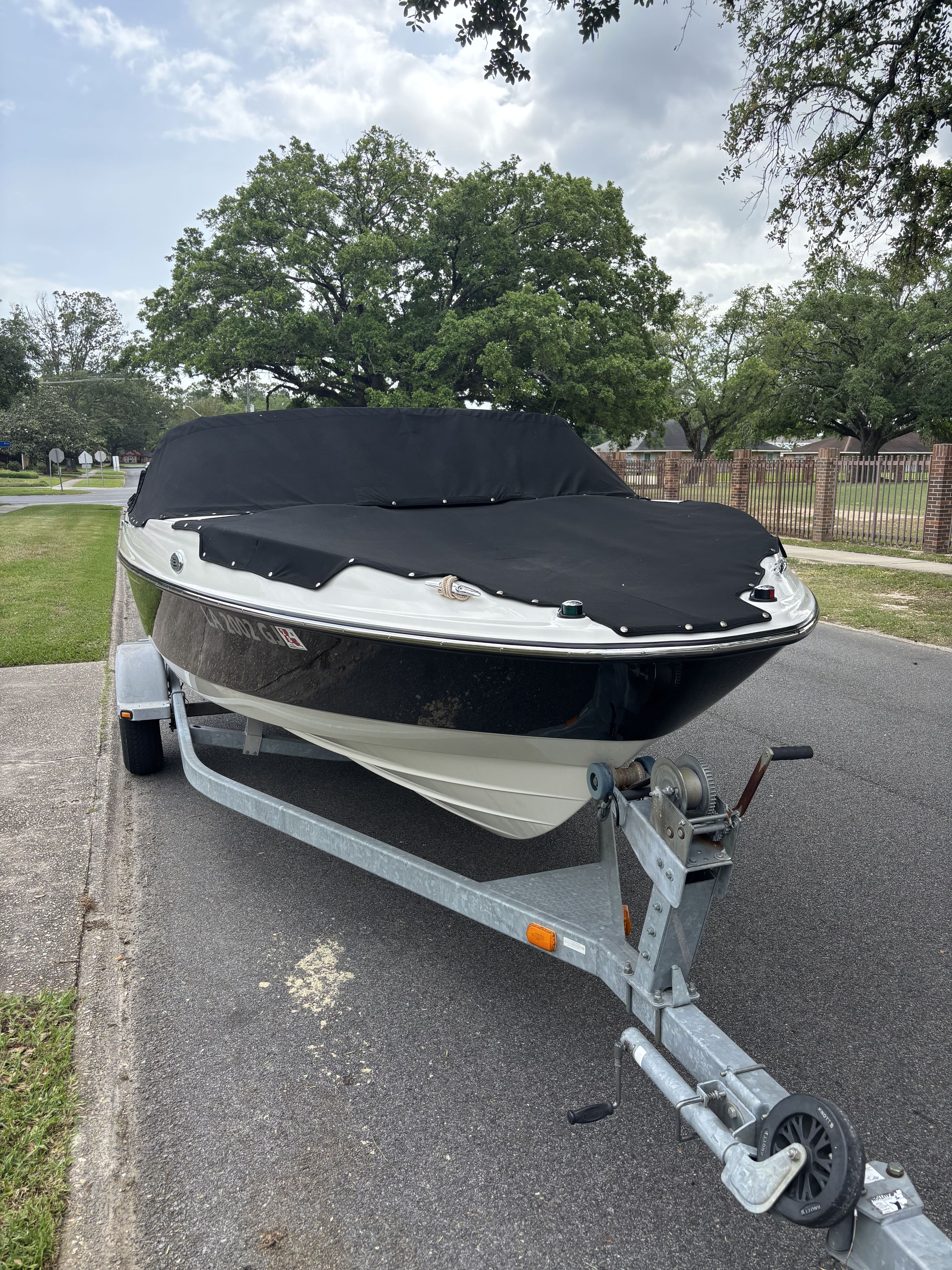 A Bayliner 215 Bowrider boat on a trailer, covered, parked on a street.
