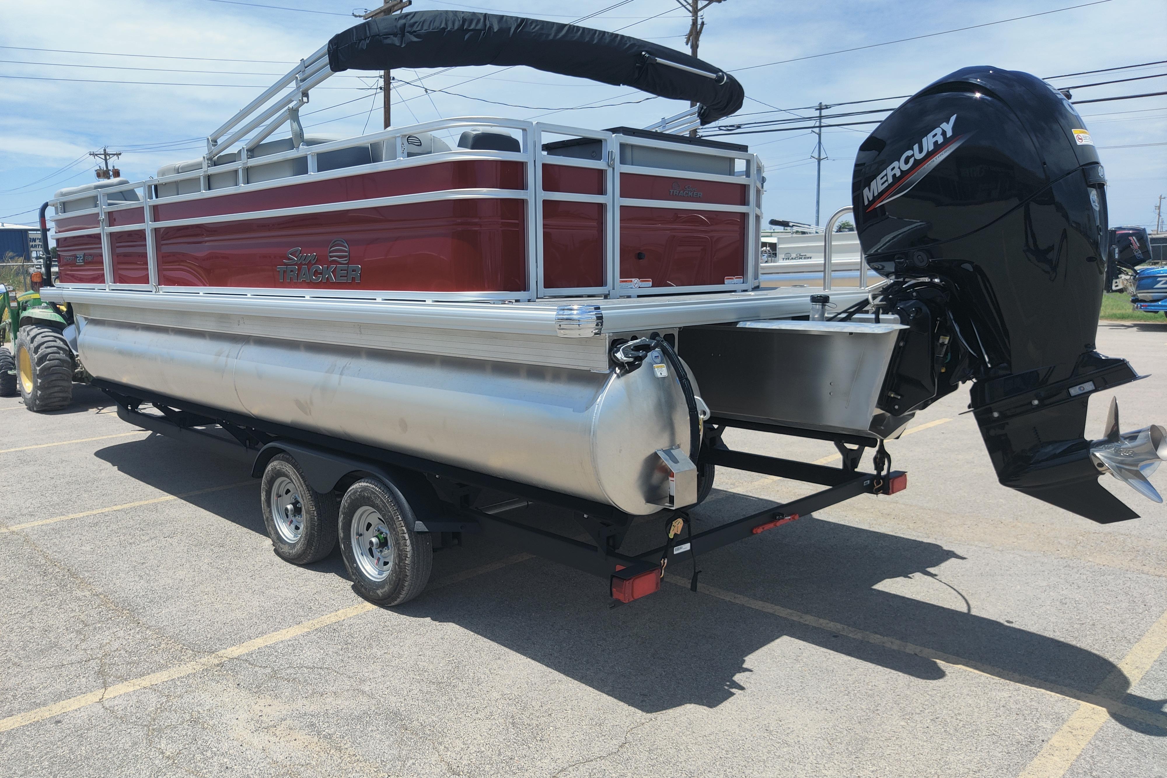 2026 Sun Tracker SportFish 22 DLX pontoon boat with Mercury outboard motor in a parking lot.