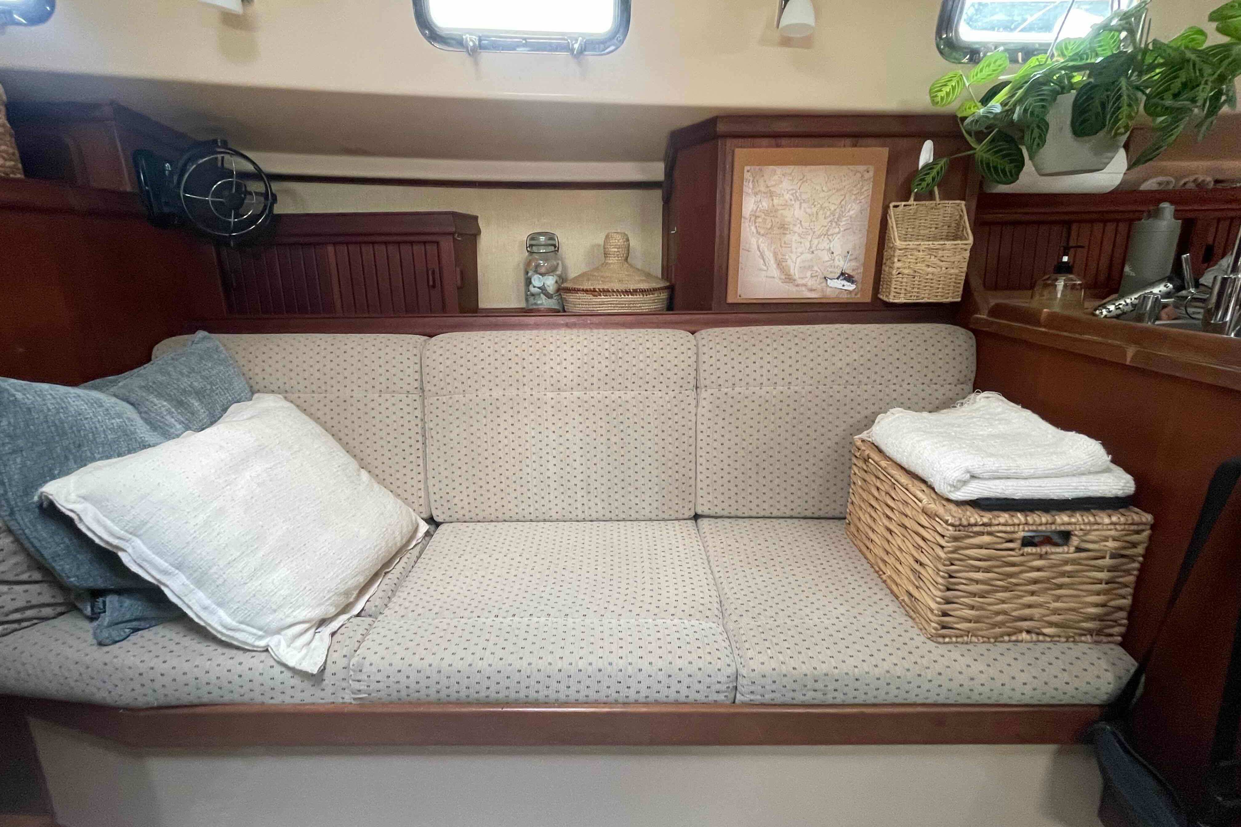 Cozy interior of 1989 Island Packet 35 sailboat with cushioned seating and wicker basket.