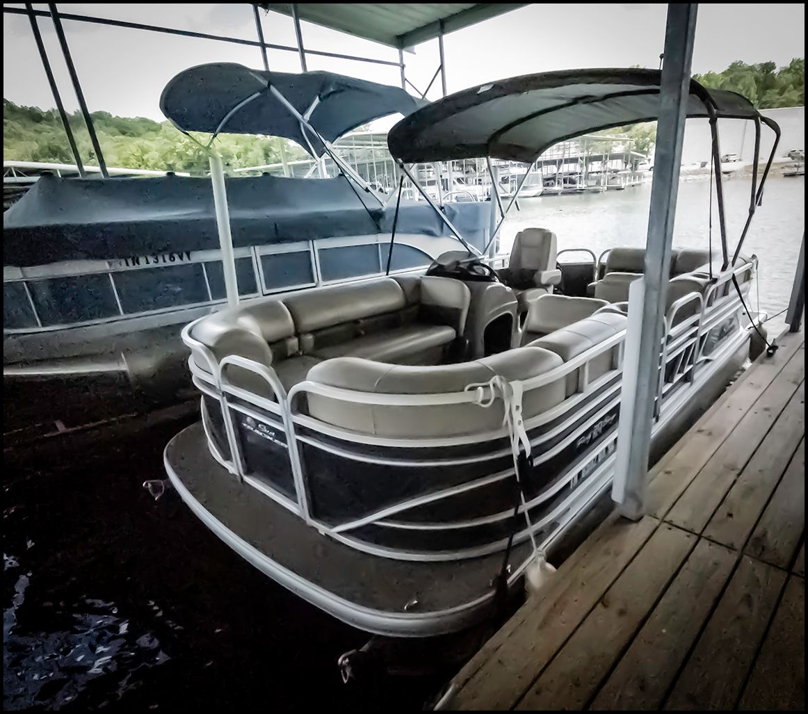 A 2023 Sun Tracker Party Barge 20 DLX docked under a covered area.