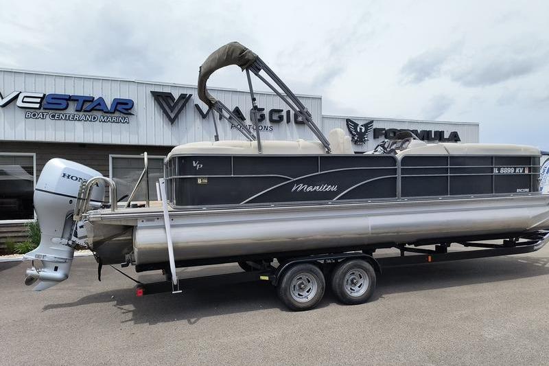 2017 Manitou 25 Oasis SE pontoon boat on trailer, parked outside dealership.