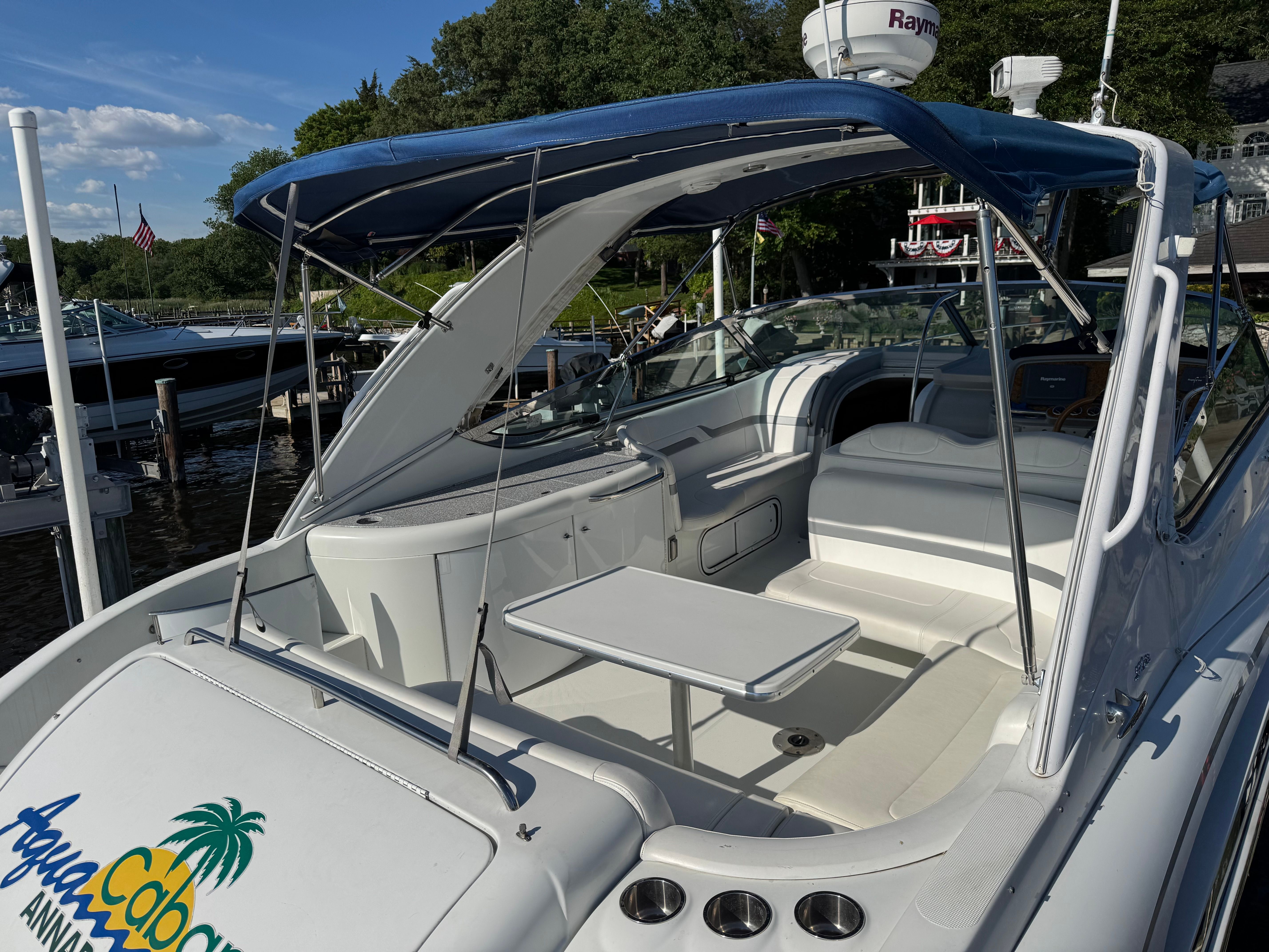 A white motorboat with a blue canopy and seating area docked at a marina.