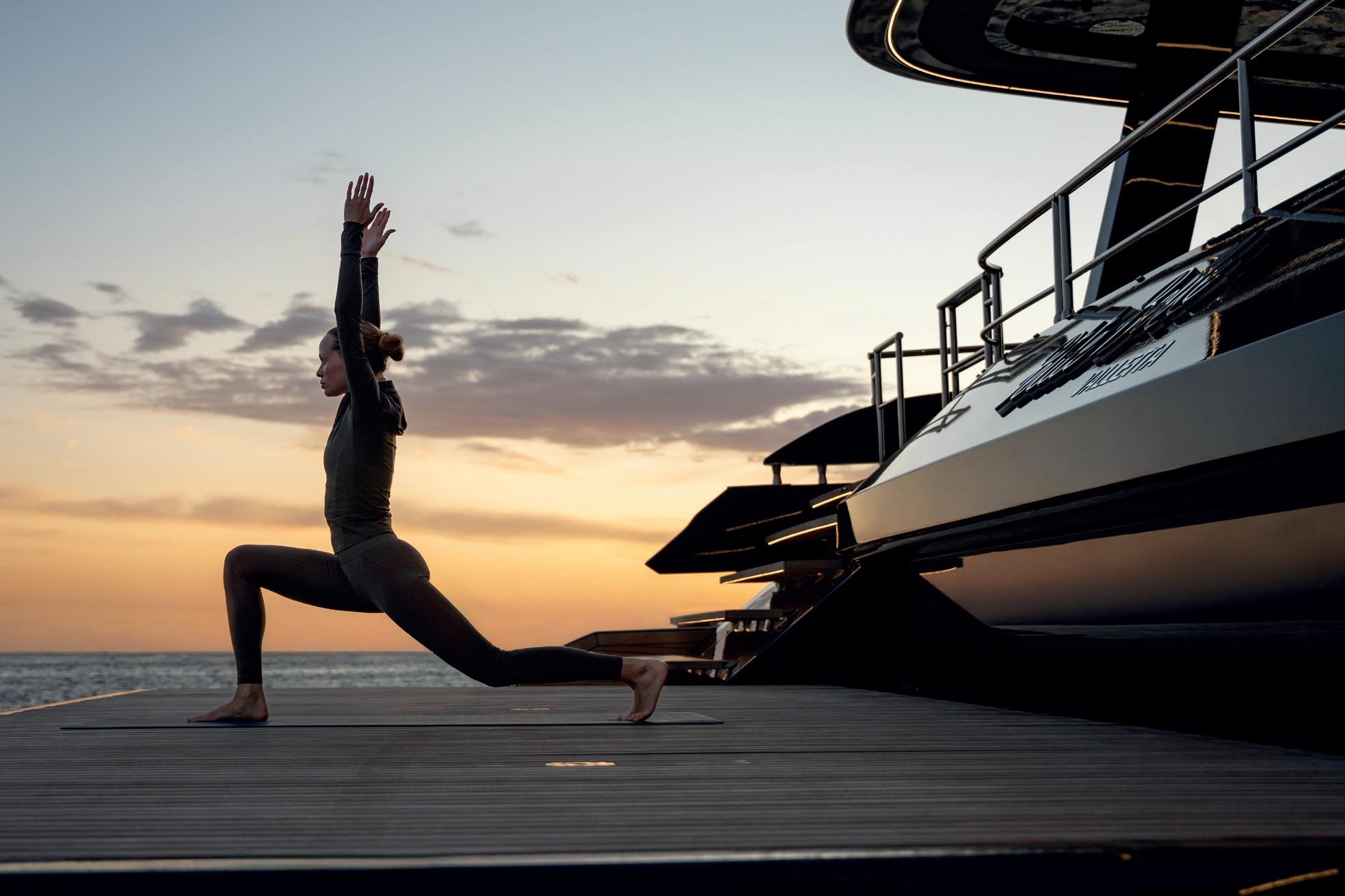 Woman practicing yoga on Sunreef 70 NEXT yacht at sunset, 2027 model.
