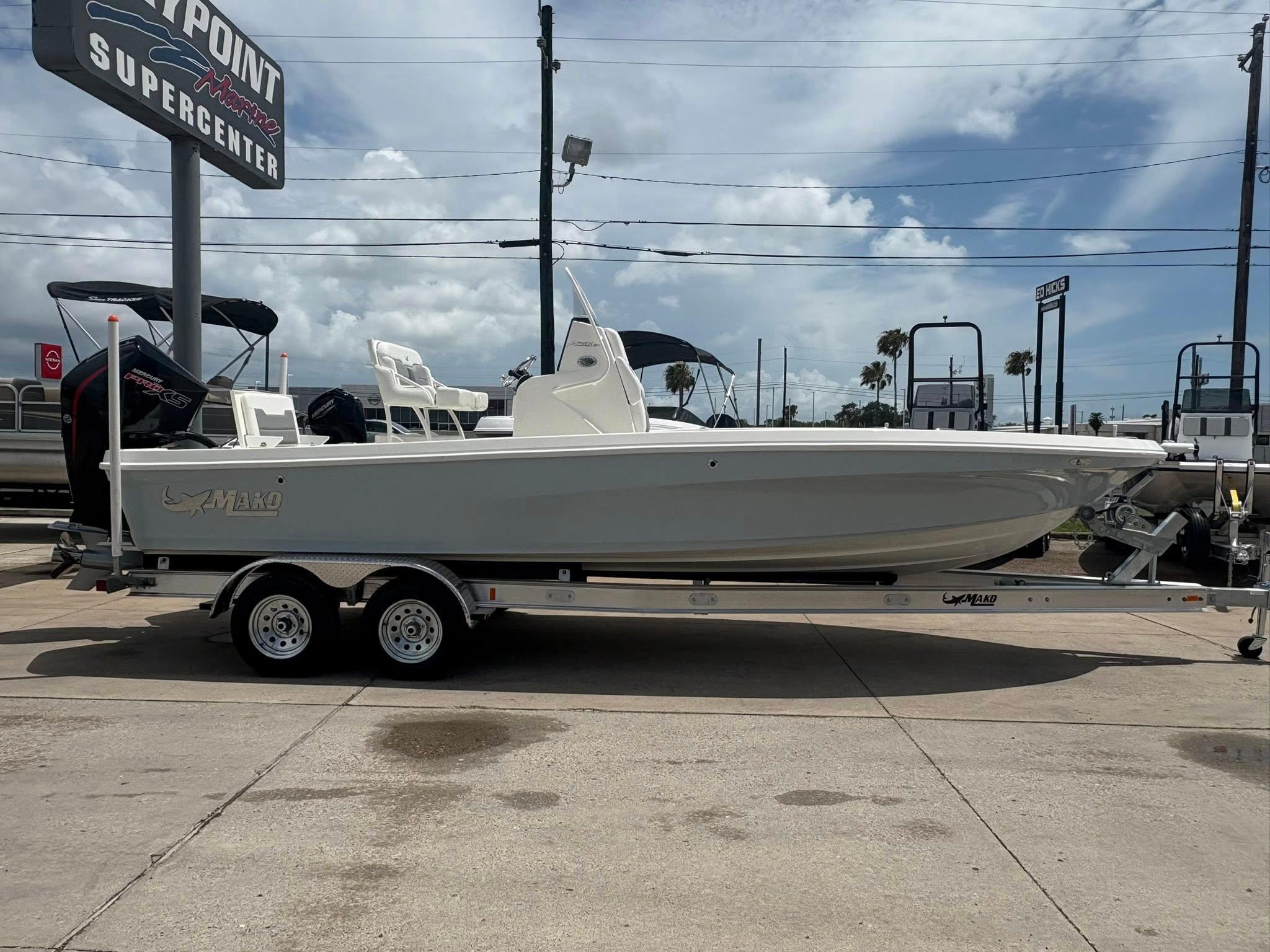 2025 Mako 24 APEX boat on trailer at dealership under cloudy sky.