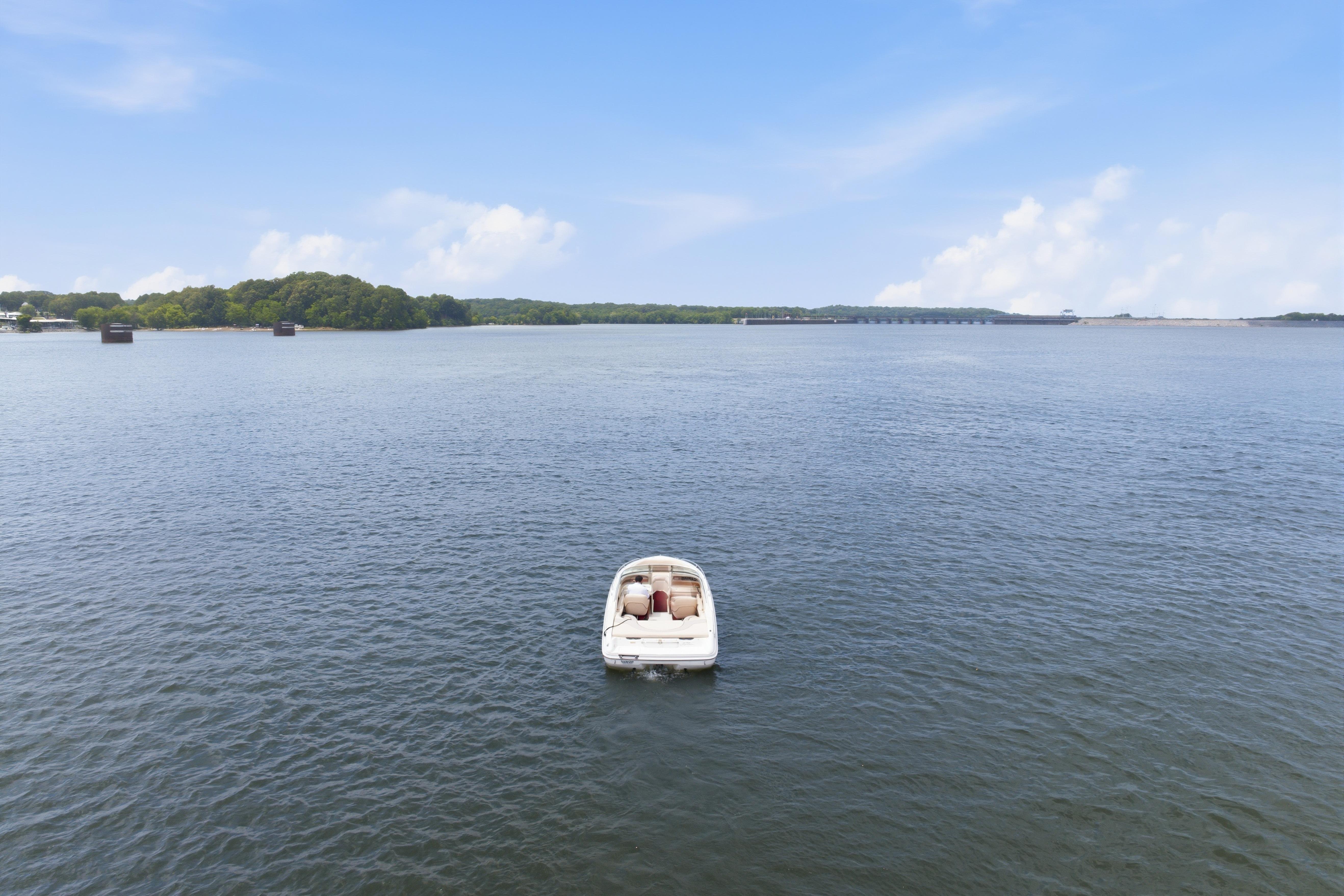 A 1997 Sea Ray 230 Signature boat on a calm lake under a clear blue sky.
