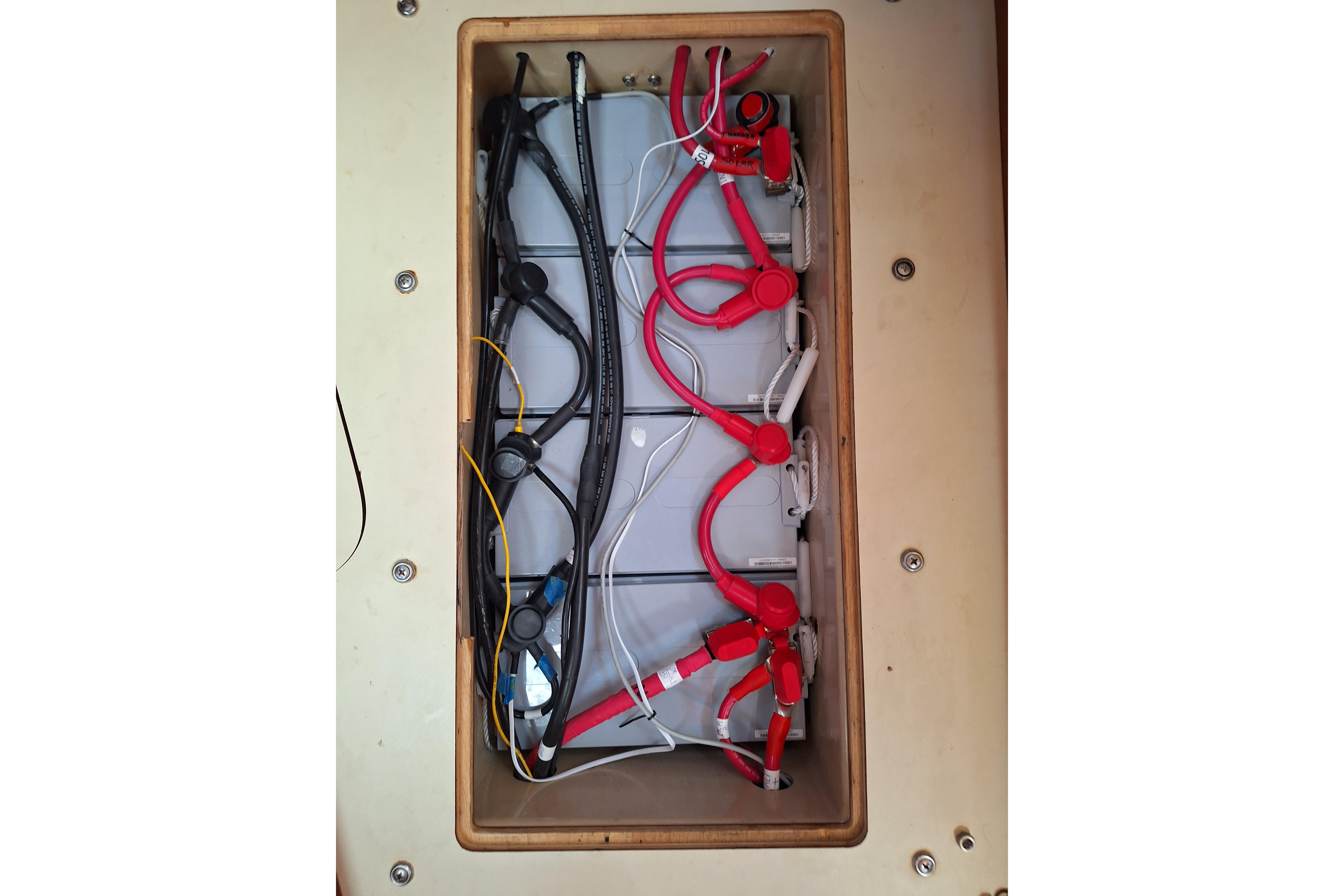 Battery compartment of a 1996 Island Packet 40 sailboat with red and black cables.