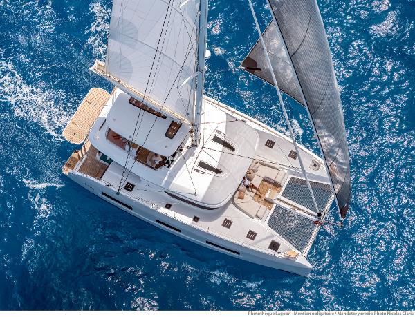 Aerial view of 2025 Lagoon 55 catamaran sailing on blue ocean waters.