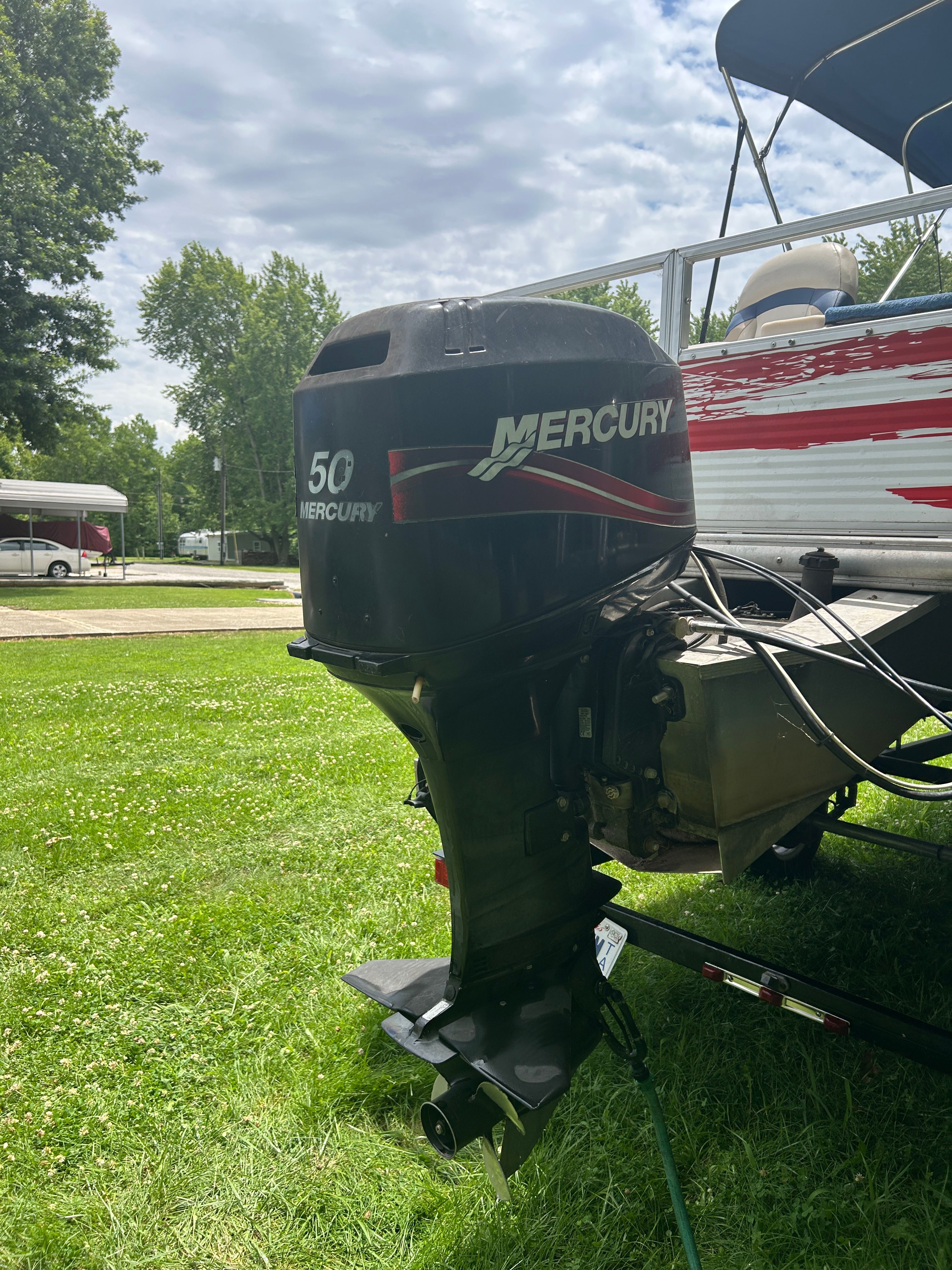 A Mercury 50 outboard motor on a 2008 Sun Tracker Fishin' Barge 21', parked on grass.