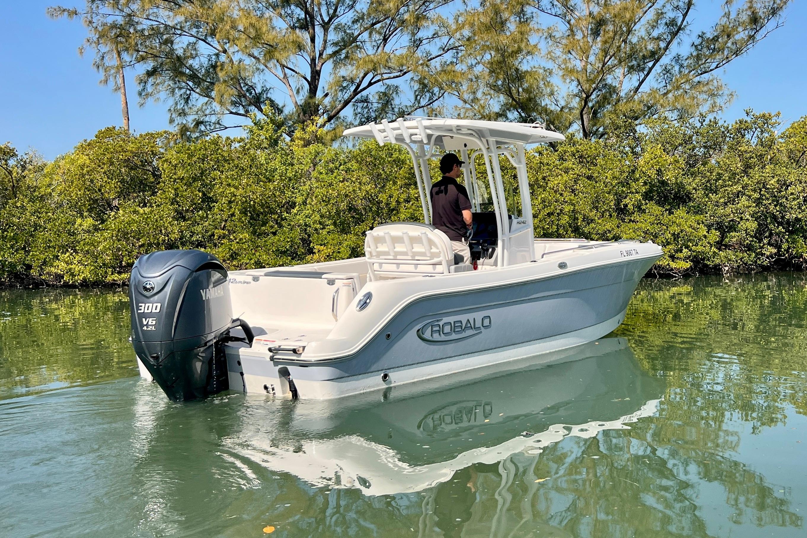 2021 Robalo R242 Explorer boat cruising in calm waters near lush greenery.