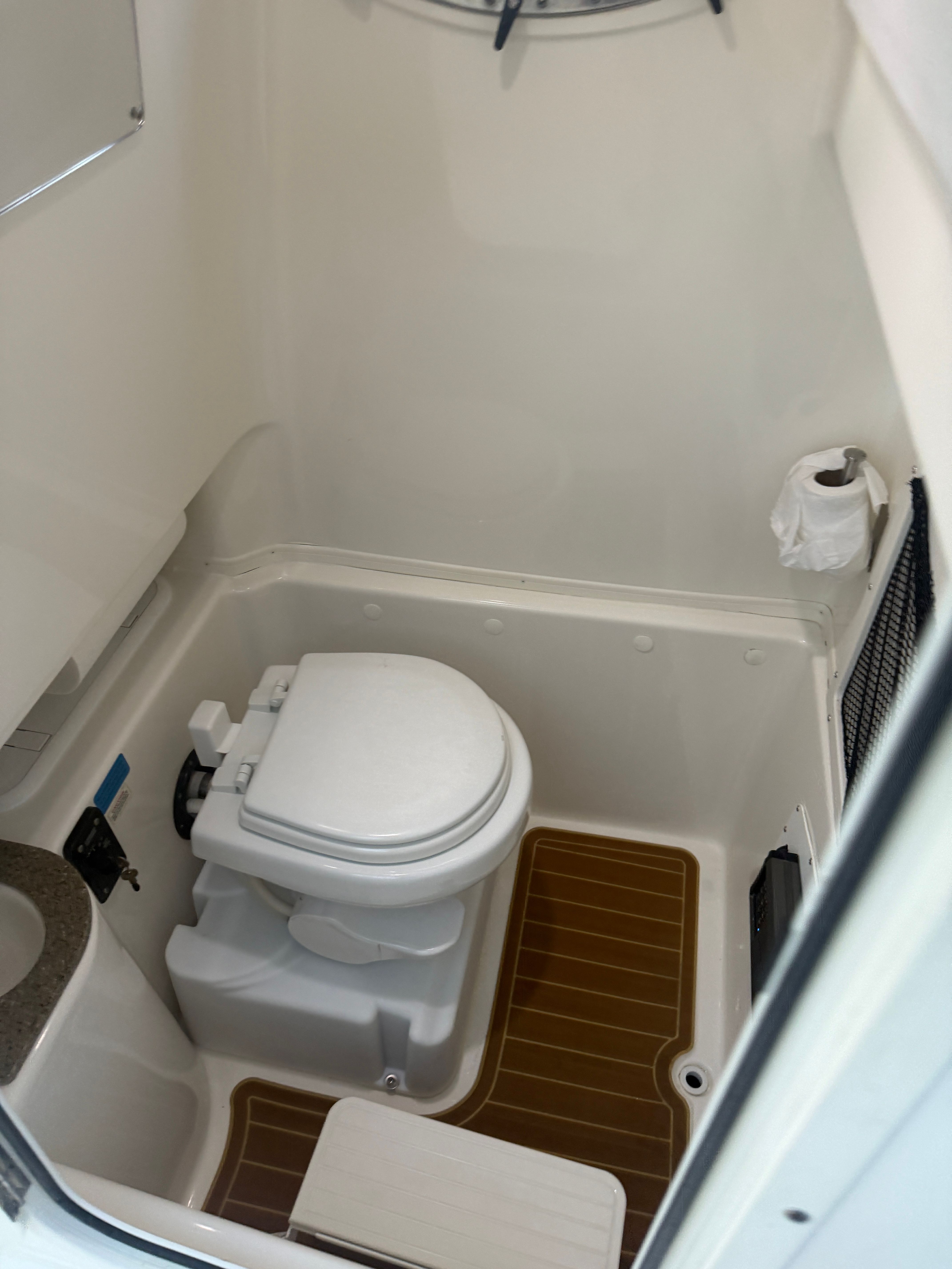 The image shows a compact boat toilet with a white toilet, brown flooring, and a sink.