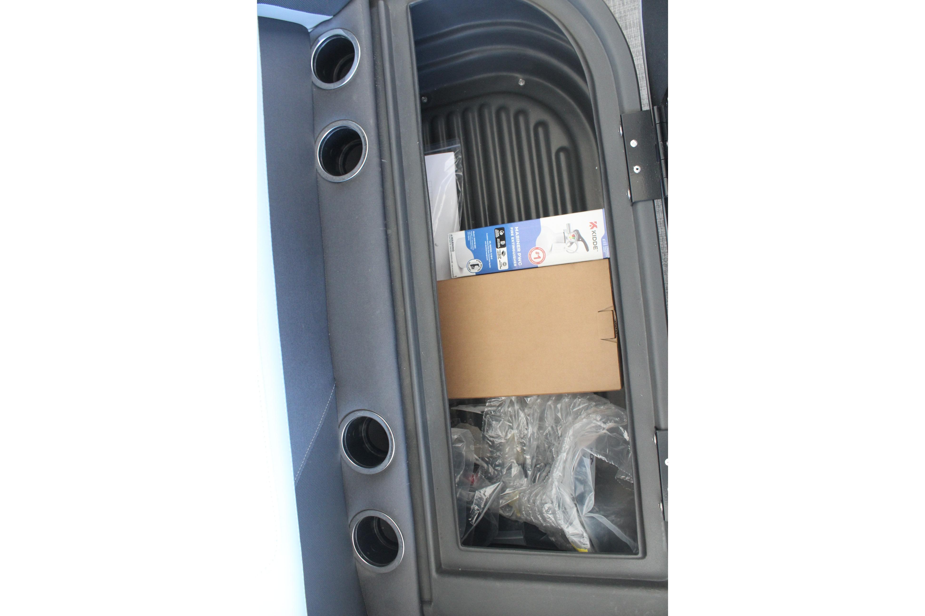 Storage compartment of 2026 Sun Tracker Party Barge 16 DLX with cup holders and packaged items.