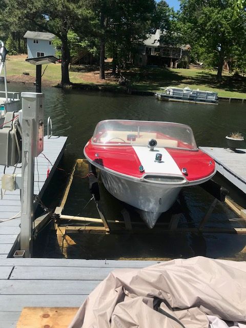 A red and white boat docked on a lake, surrounded by trees.