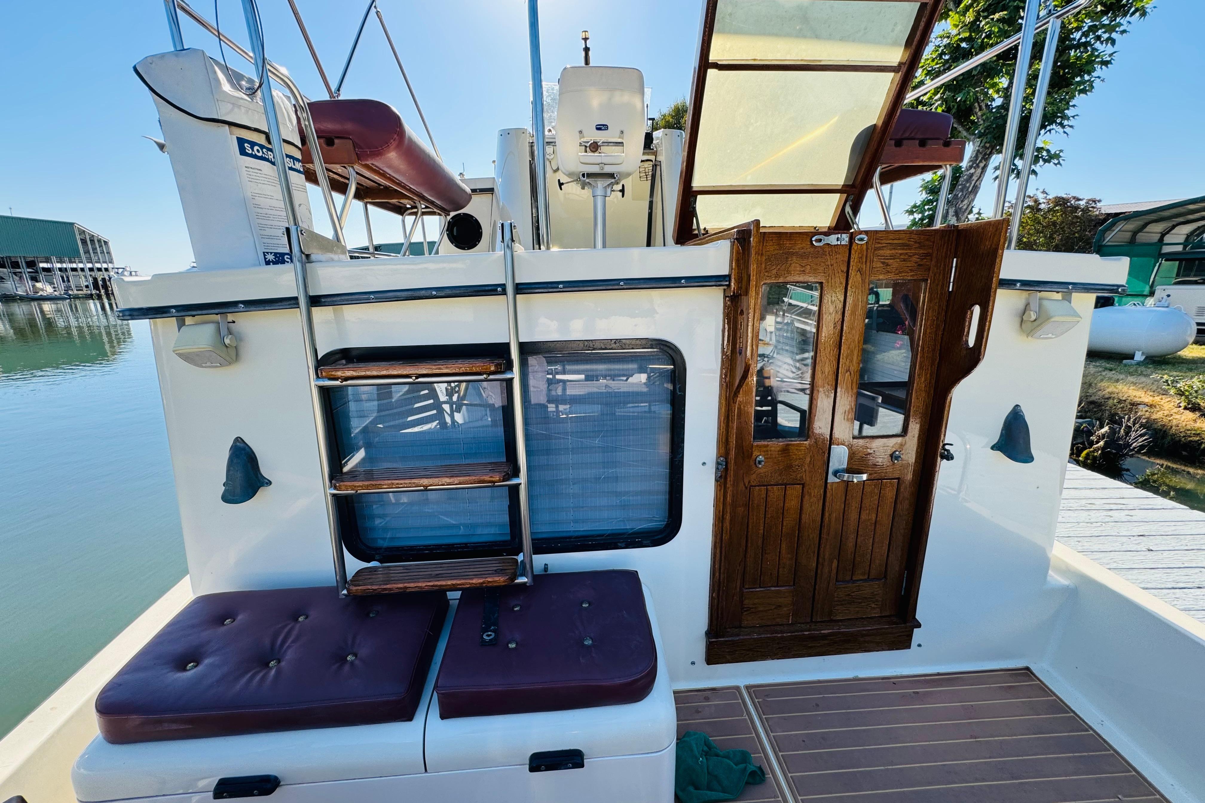 1996 Nordic Tug 32 boat with wooden doors, ladder, and cushioned seating on deck.