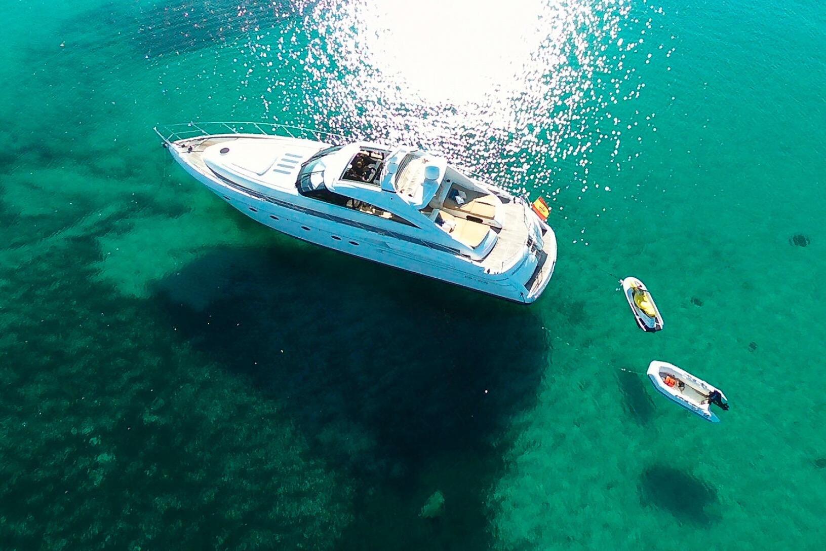 Aerial view of 2001 Princess V65 yacht on clear turquoise water with small boats nearby.