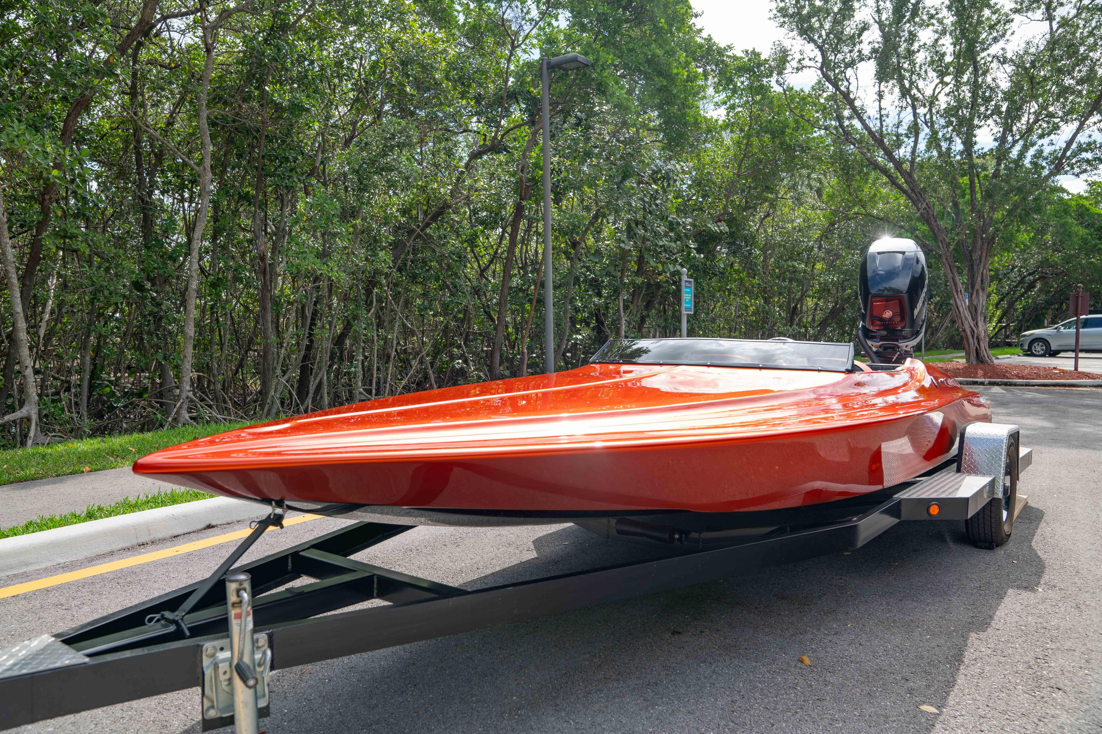 1984 Sleekcraft Aristocrat 20 boat on trailer, vibrant orange finish, parked near lush greenery.