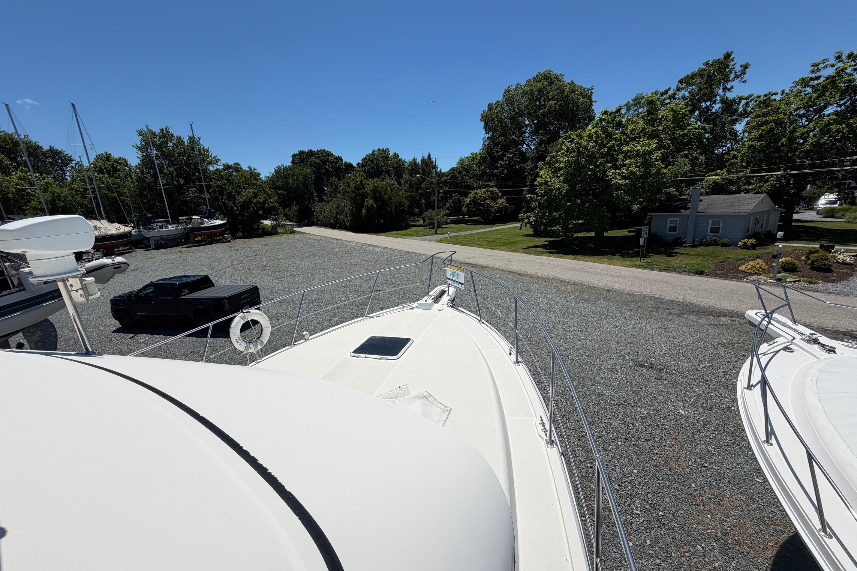 1995 Carver 356 Aft Cabin Motor Yacht on gravel lot, surrounded by trees and parked vehicles.