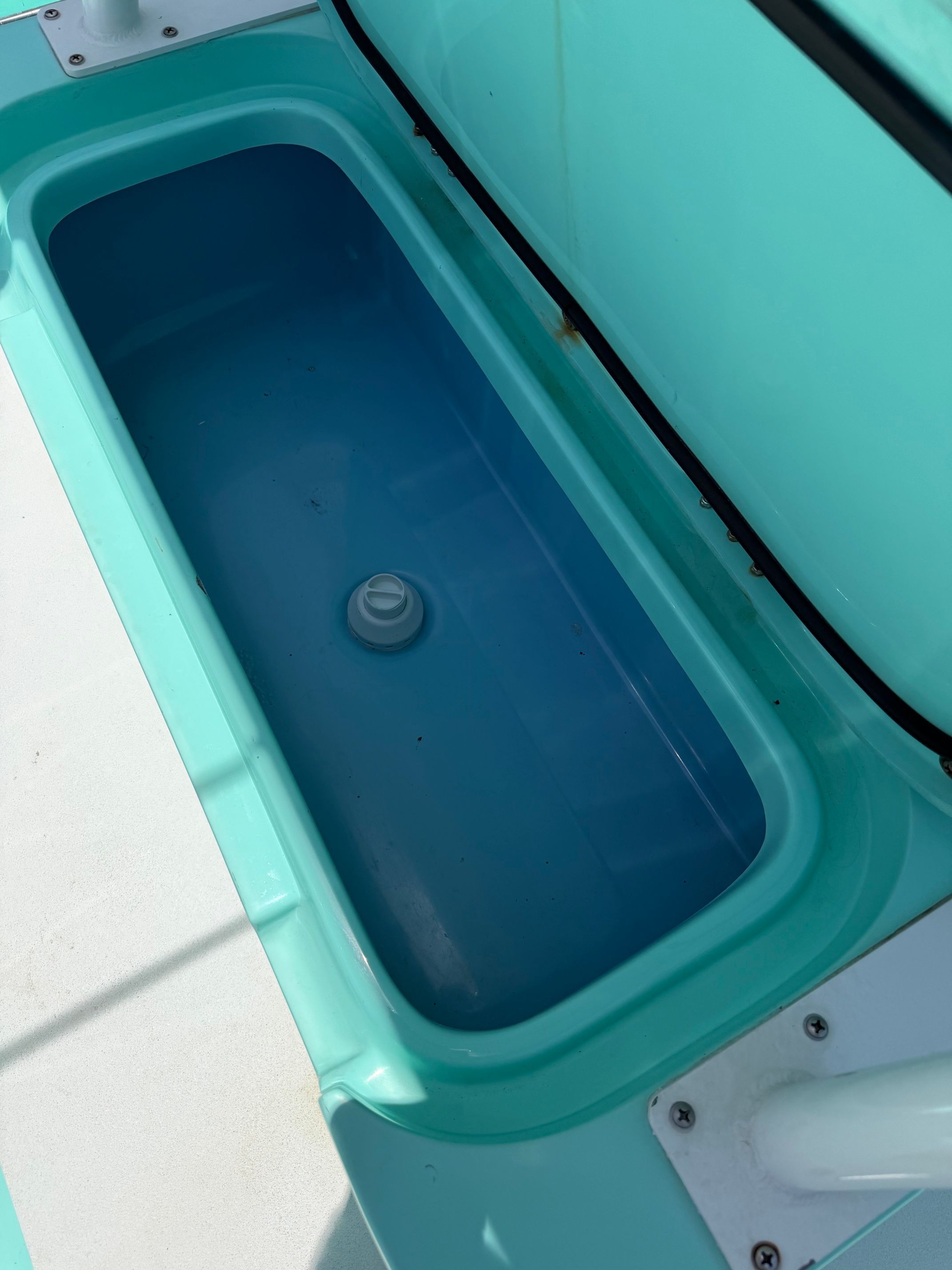 A turquoise storage compartment on a boat with a round drain in the center.