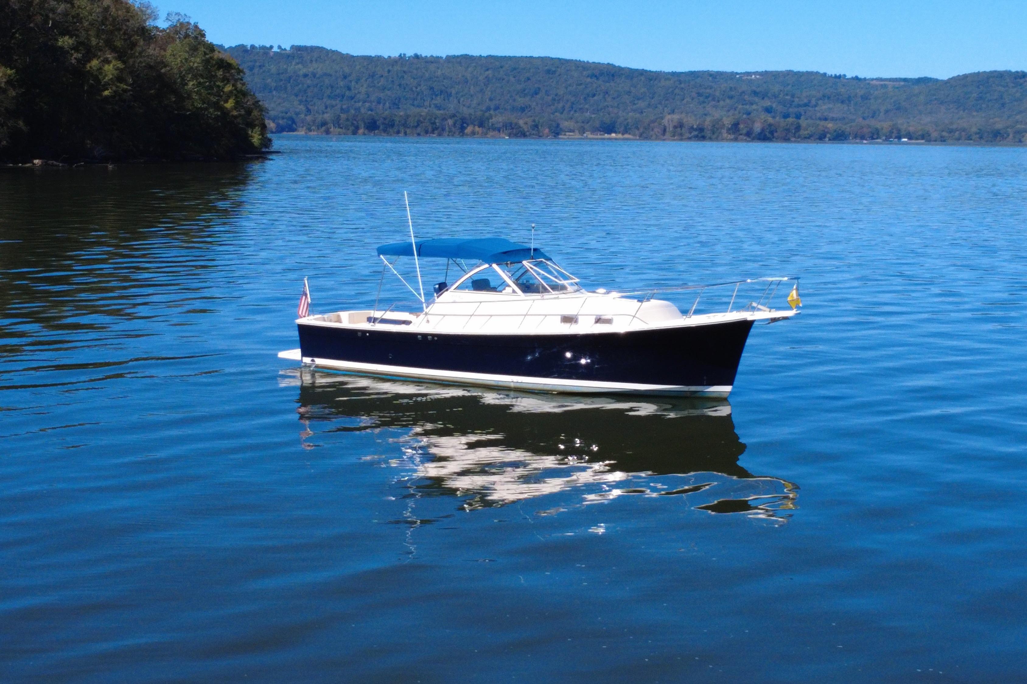 2003 Mainship Pilot 30-II boat on a serene lake with forested hills in the background.