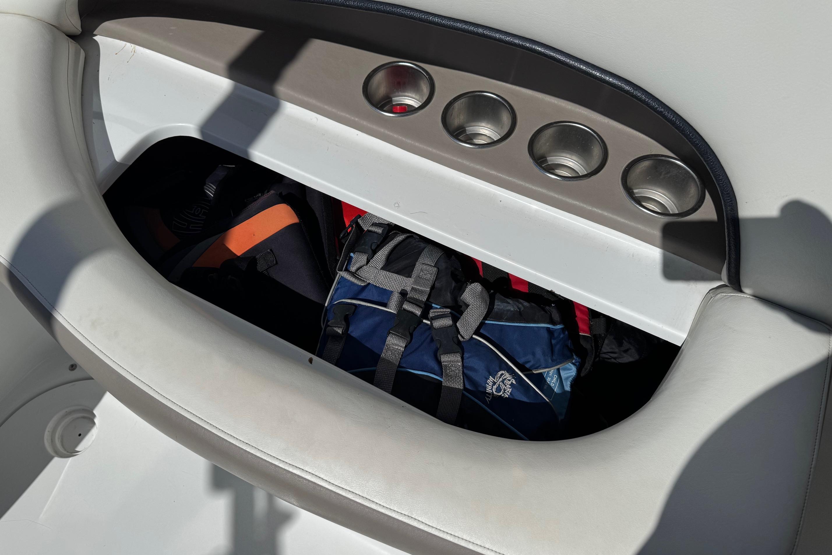 Storage compartment in a 2005 Cobalt 240 boat with bags and cup holders.