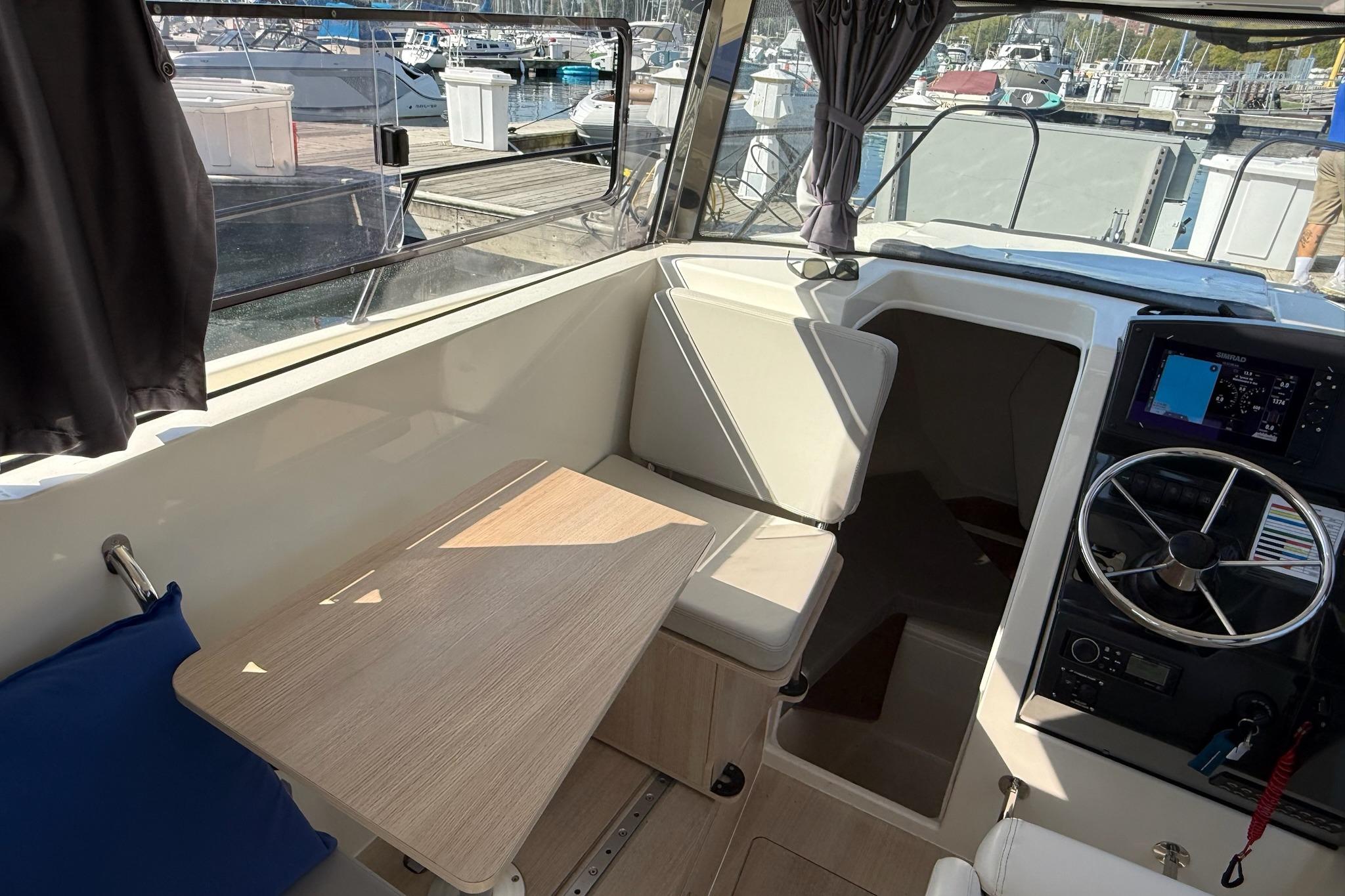 2024 Bayliner Trophy T25 Pilothouse interior with helm, seating, and table at marina.