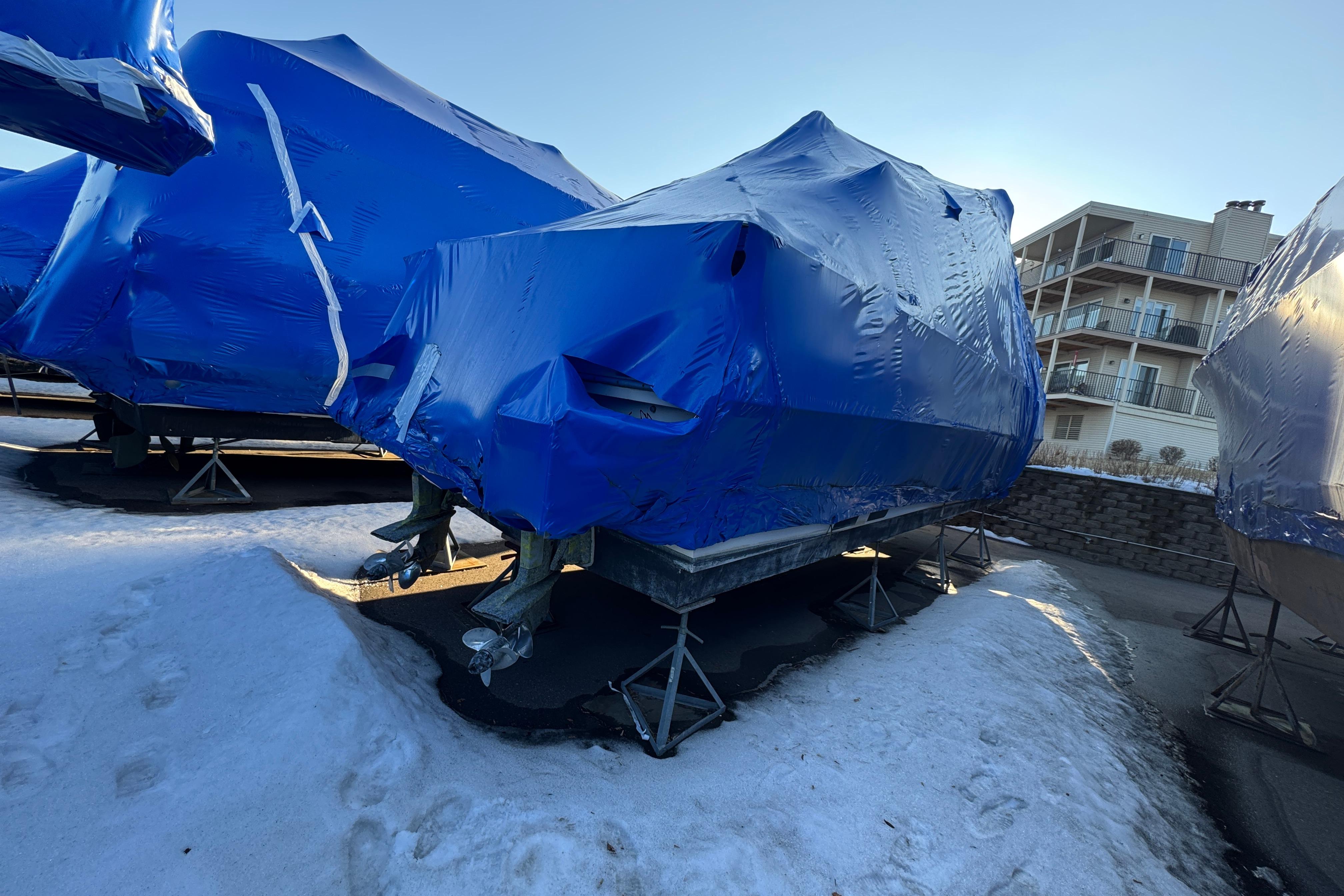 1989 Holiday Mansion Super boat covered in blue tarp, stored on stands in snowy area.