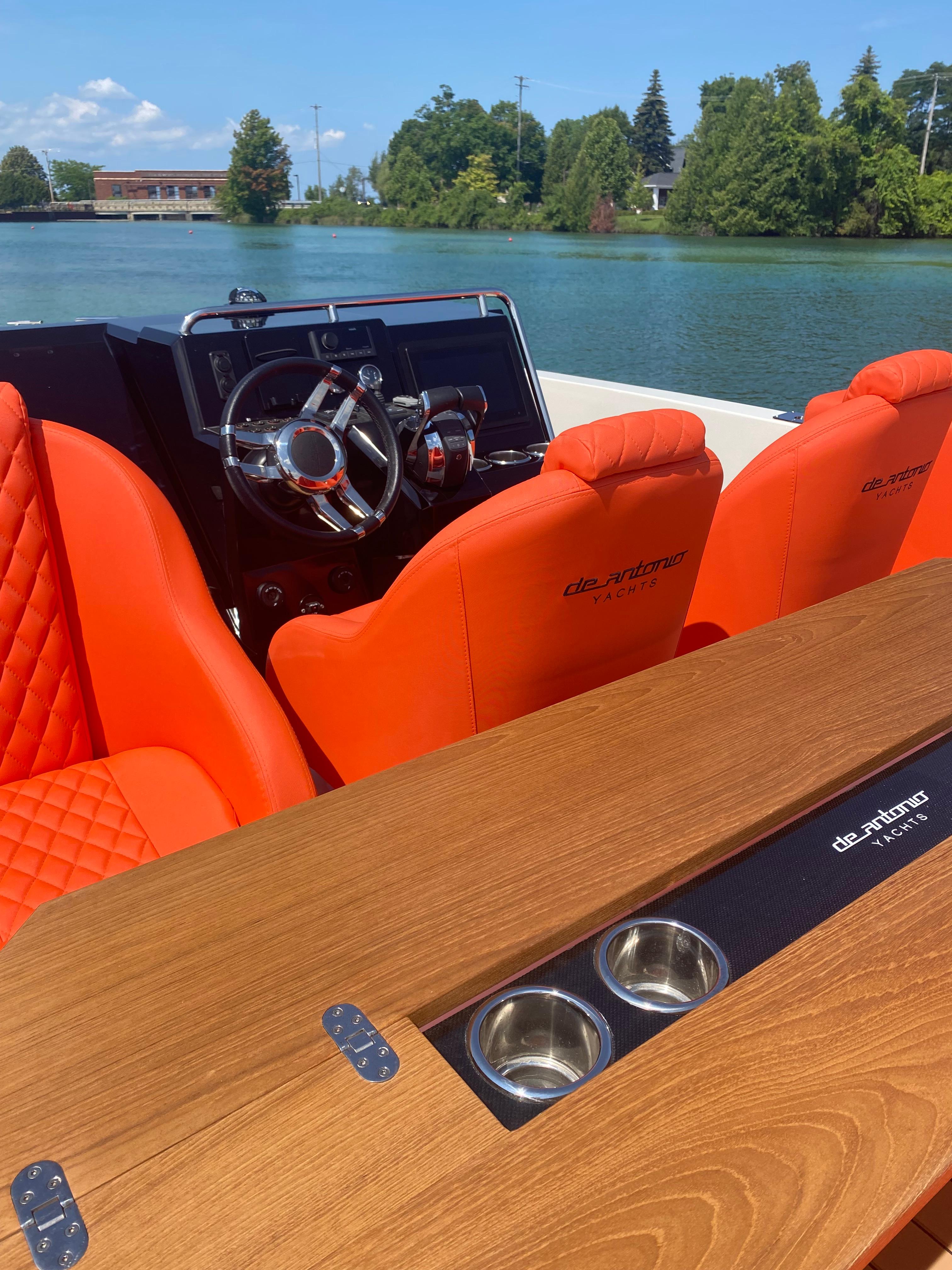 2020 De Antonio Yachts D 28 with orange seats and wooden table on a serene lake.