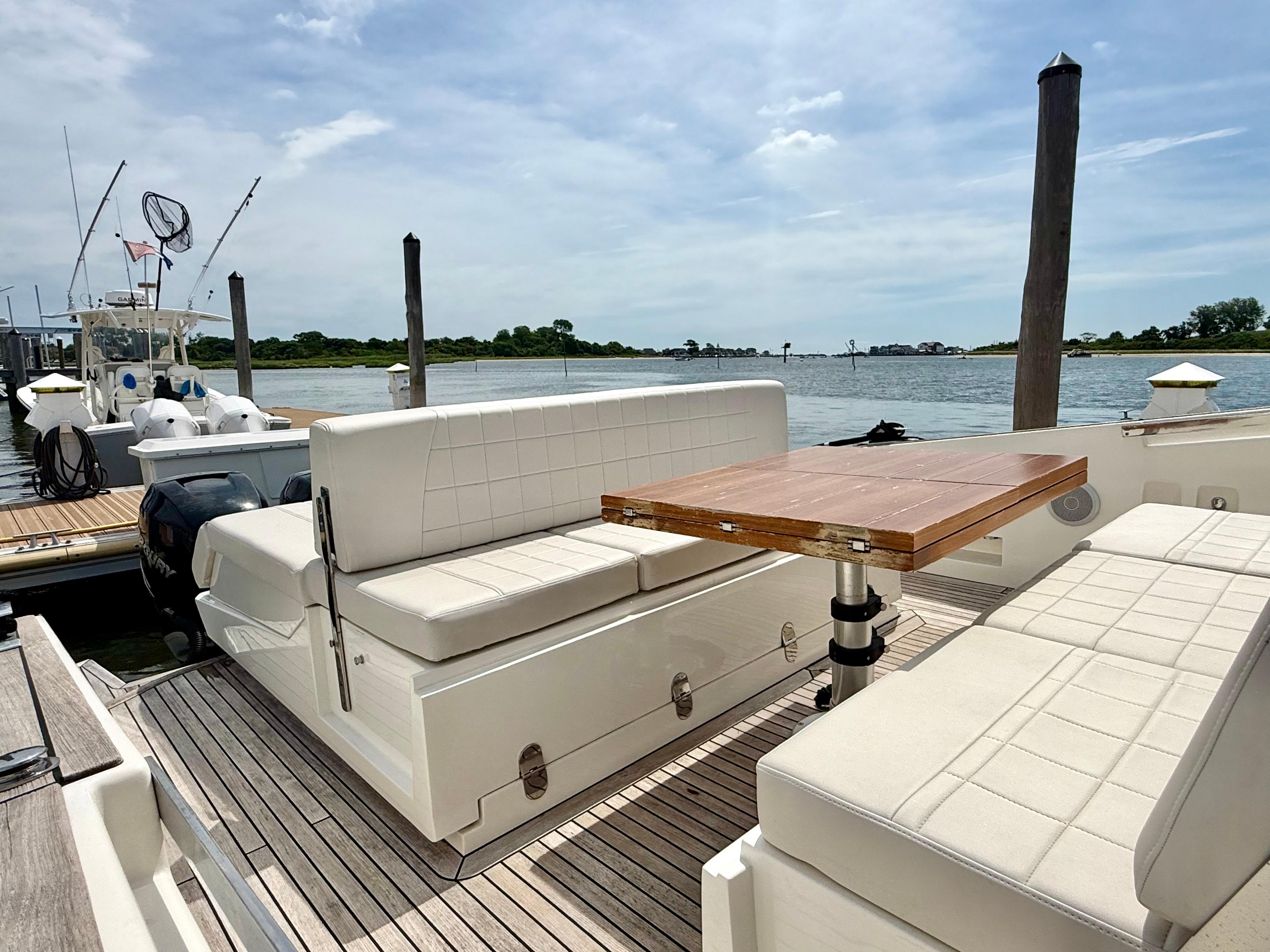 2023 Astondoa 377 Coupe Outboard, elegant seating area with wooden table, docked by the water.