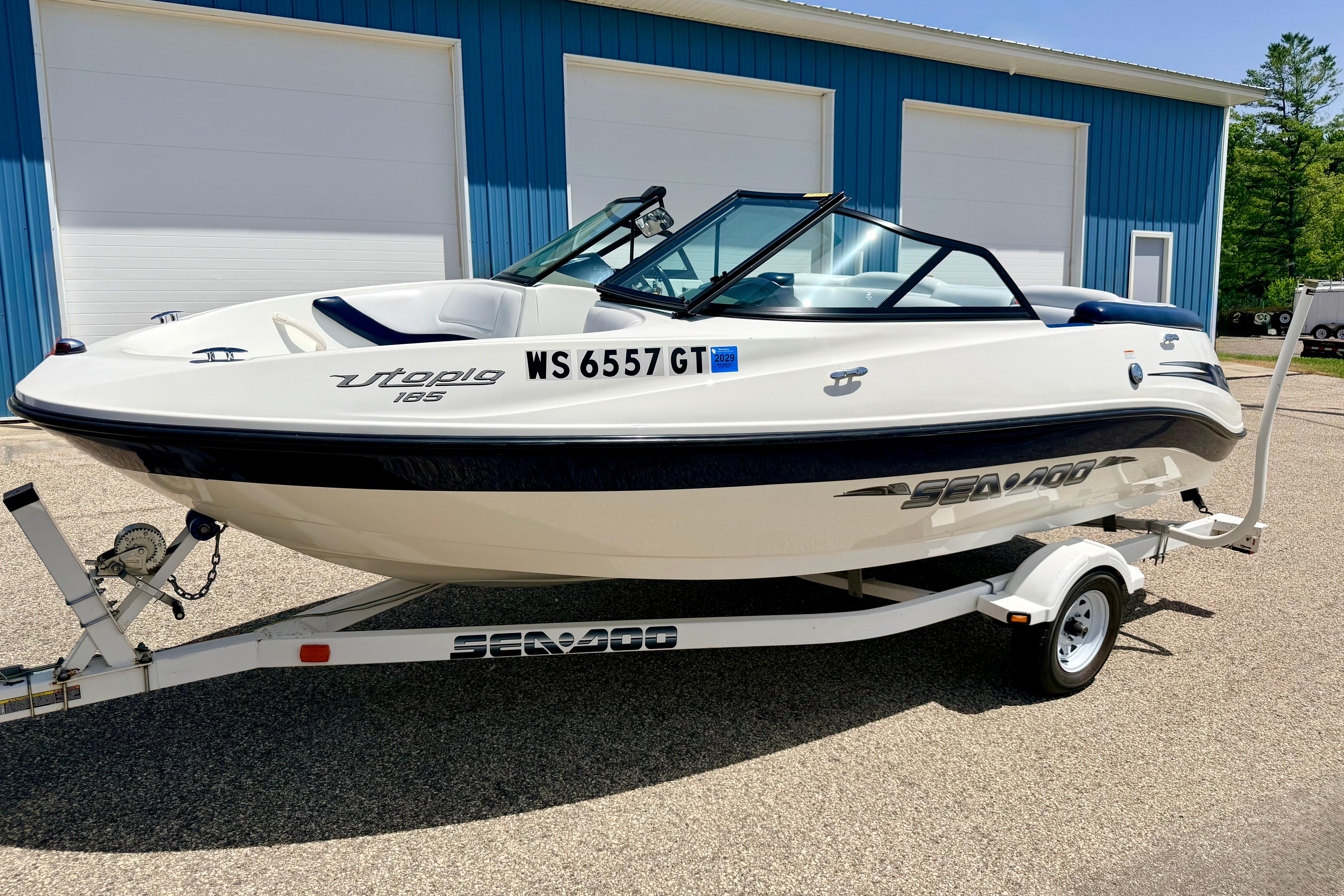 2004 Bombardier SEADOO Utopia 185 boat on trailer, parked outside blue building.
