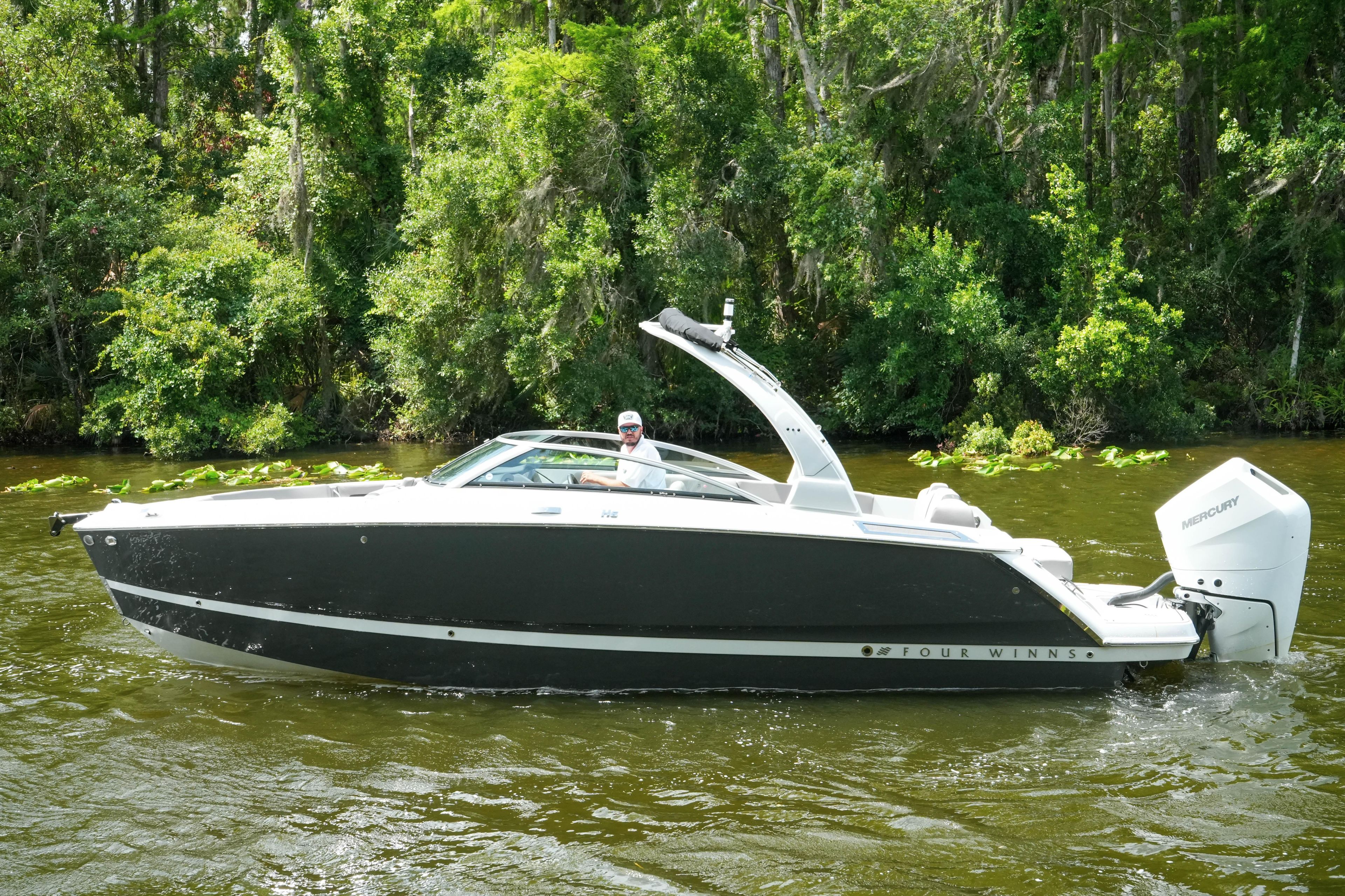 2026 Four Winns H6 OB boat cruising on a scenic river with lush greenery.