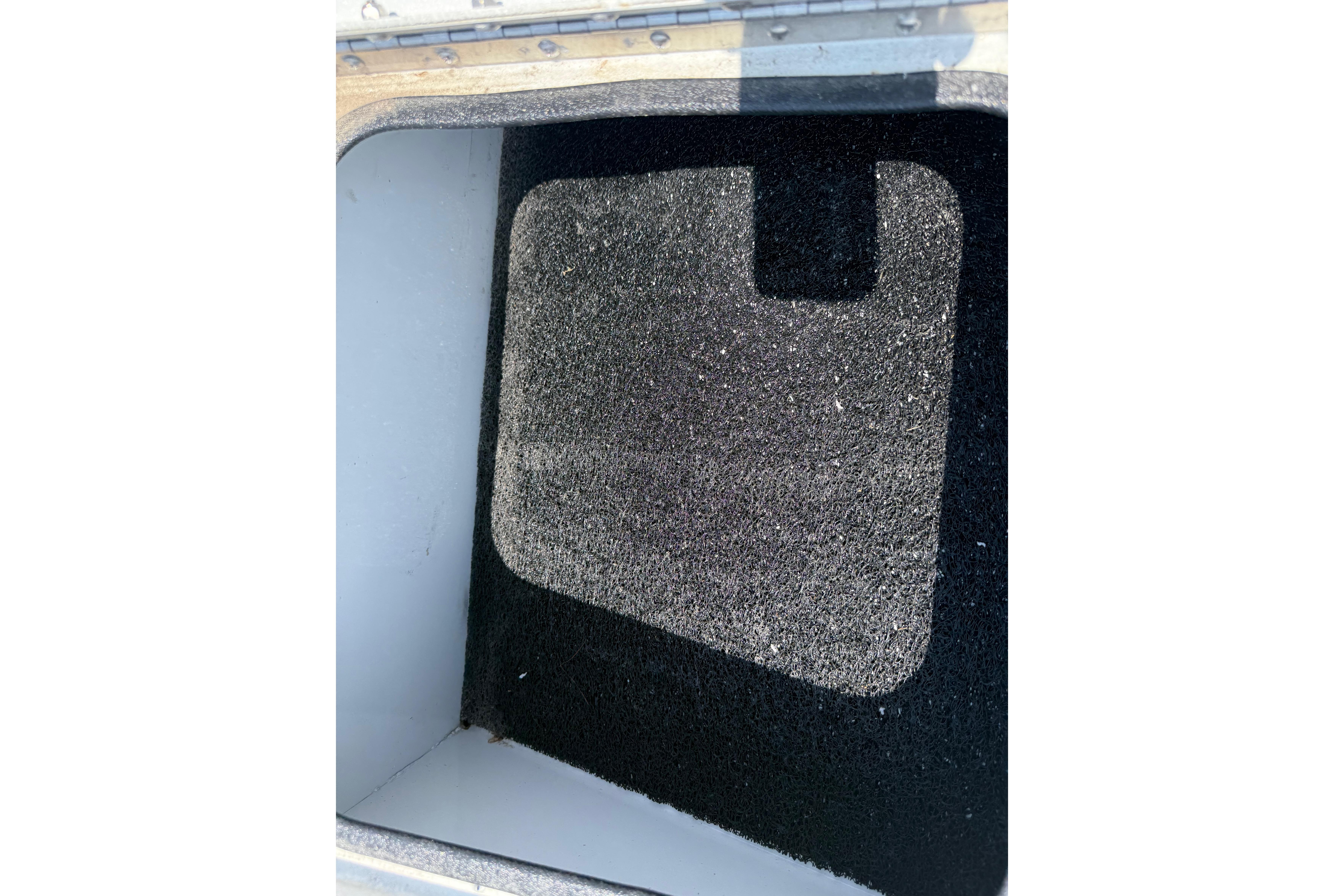 Storage compartment of 2025 Avid 22 Recon boat with black carpet lining.