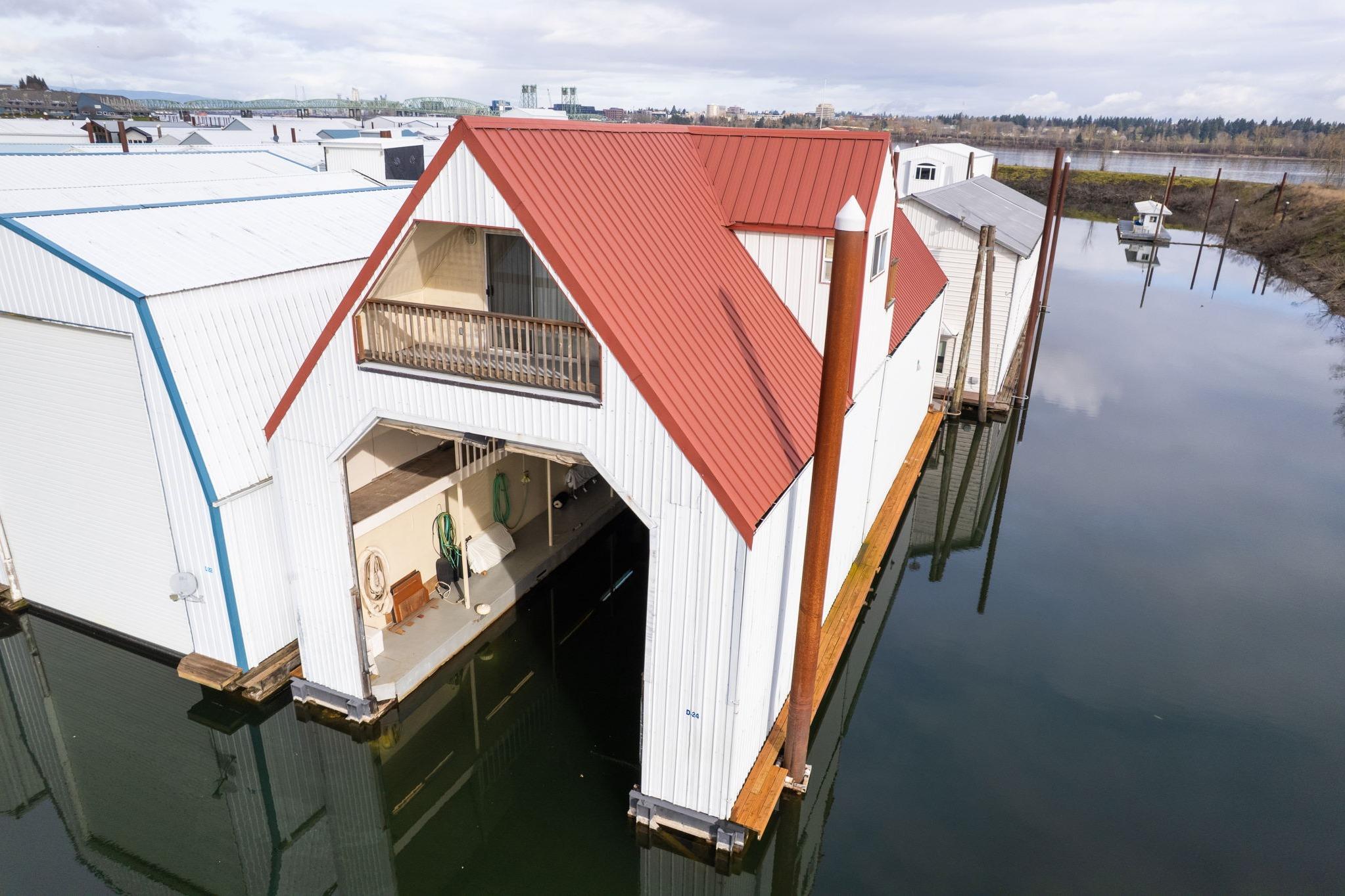 Custom 1976 boathouse with red roof, docked on calm water, featuring open garage.